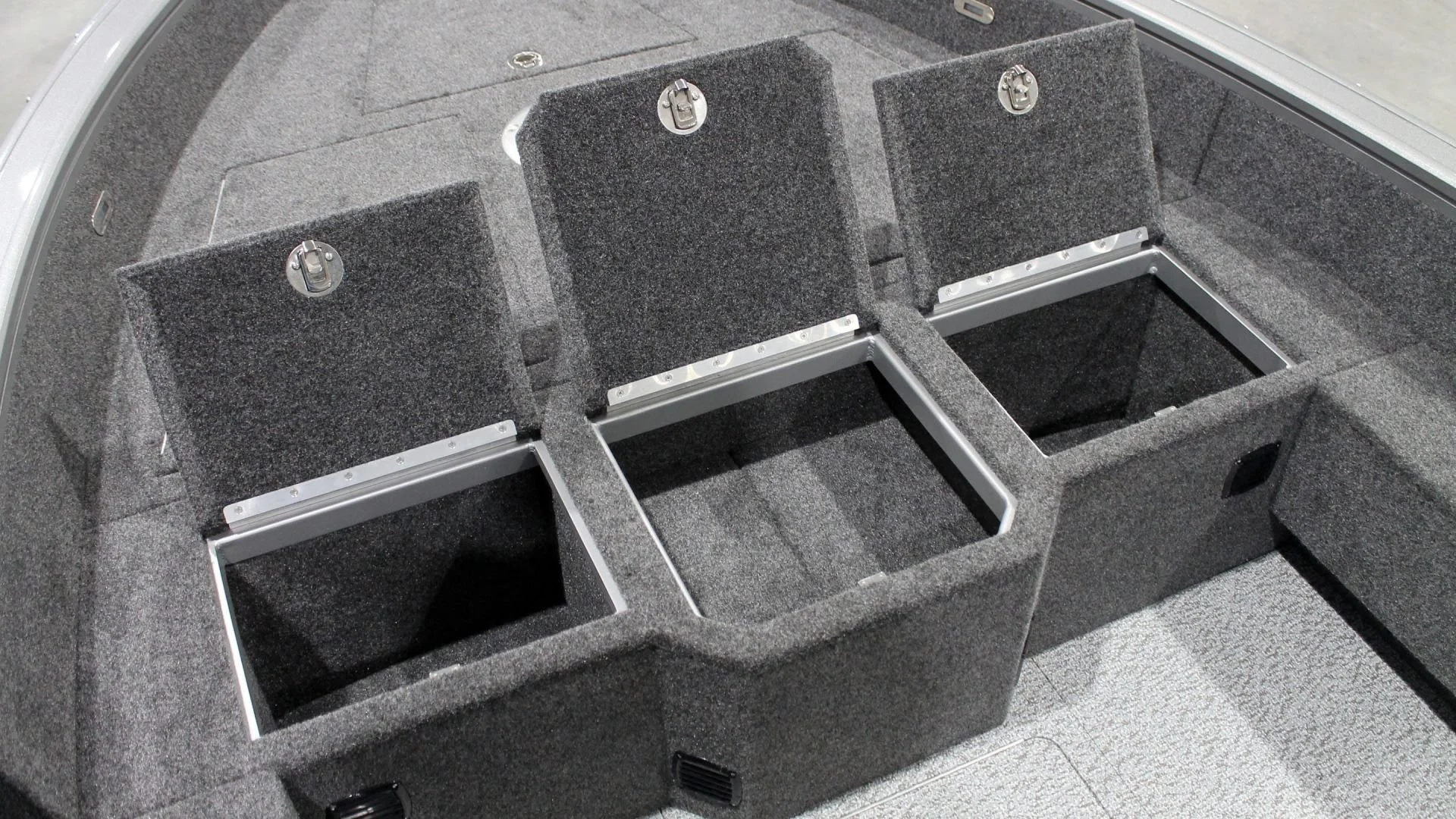 Inside of a boat with three rectangular compartments and two adjustable vertical partitions, all lined with gray carpeting.