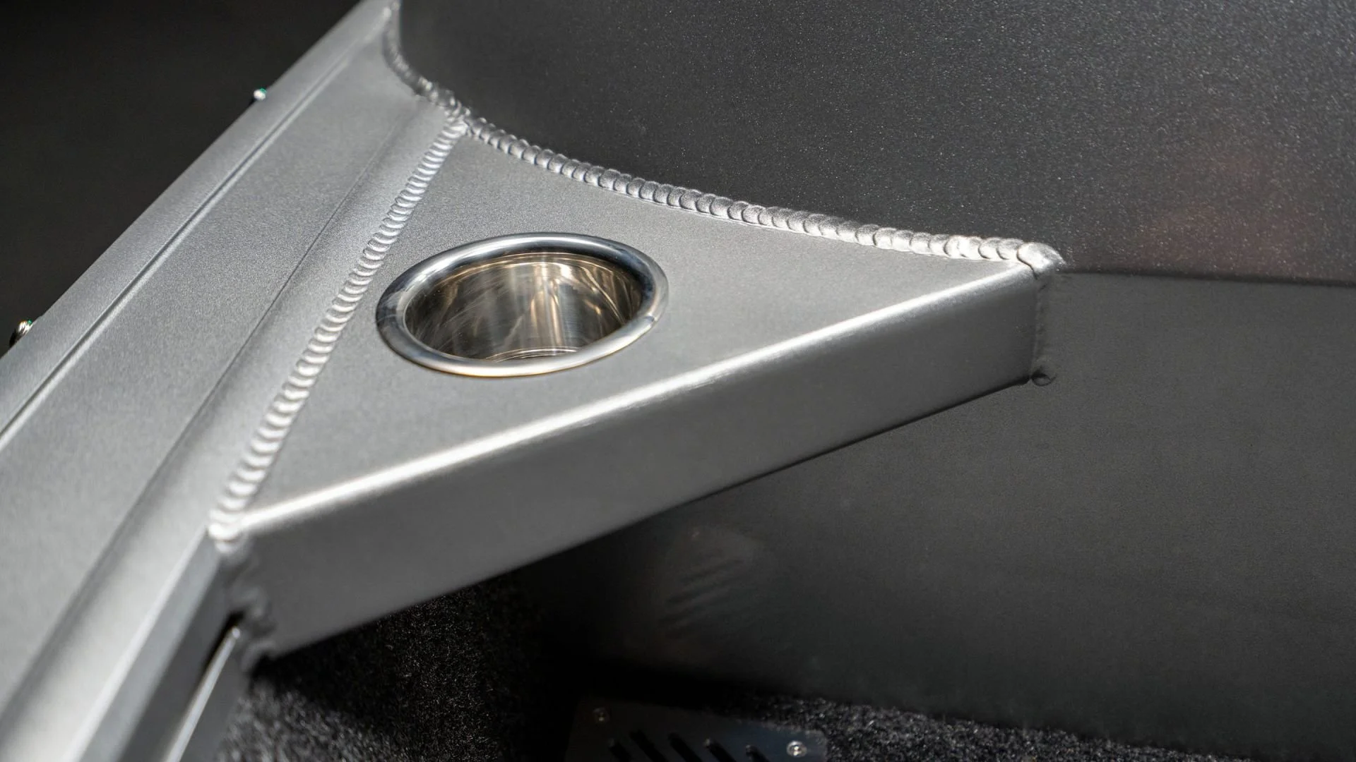 Close-up of a metallic component with a rounded recessed hole, located on a dark surface.