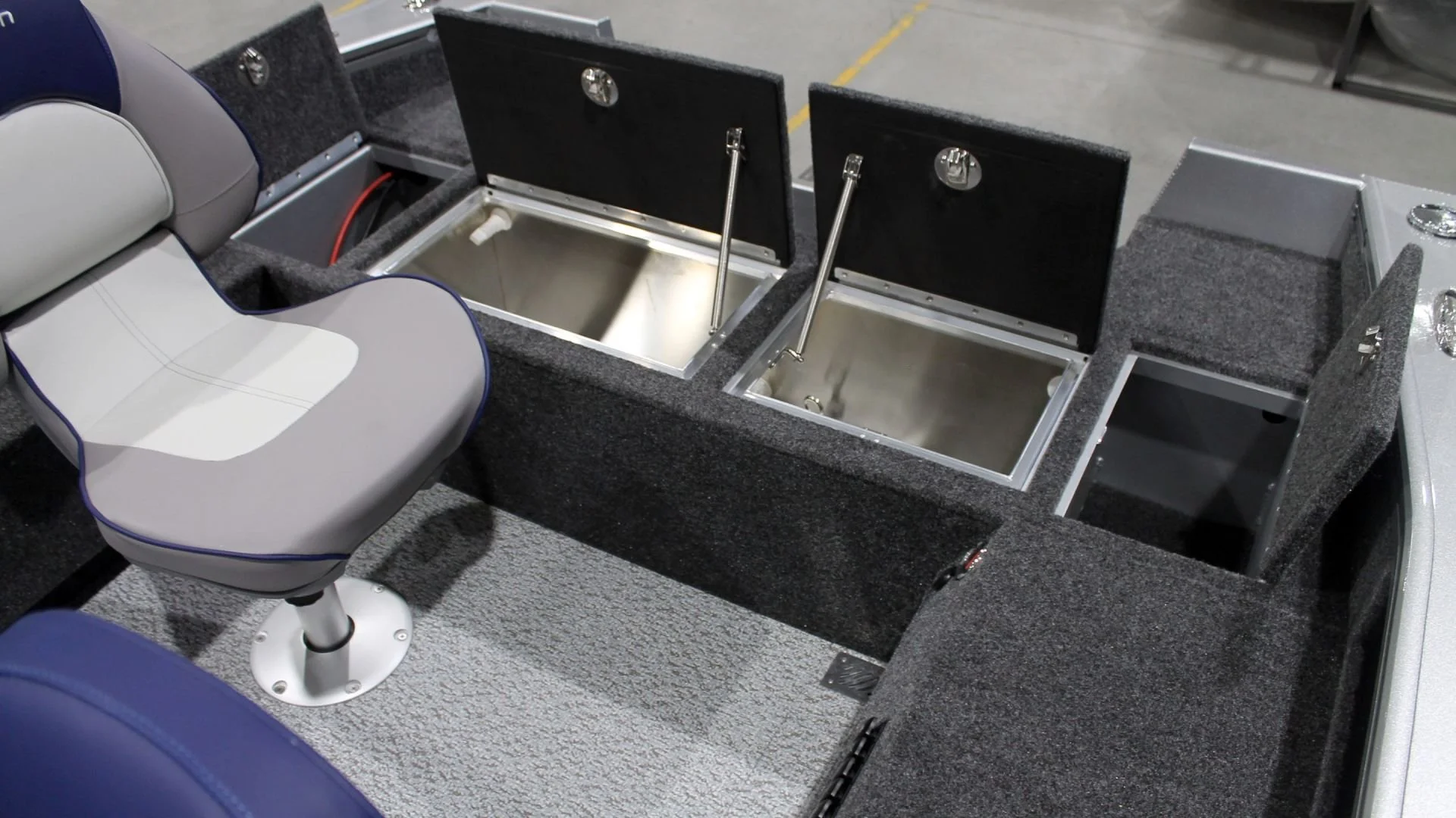 A boat interior with two open storage compartments, a padded chair, and carpeting.