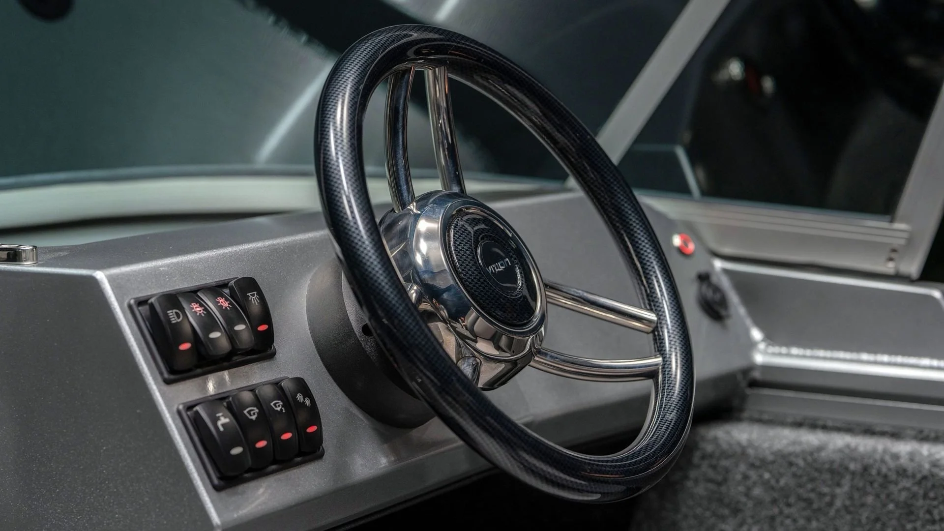 Close-up view of a vintage race car dashboard with a carbon fiber steering wheel and multiple switches.