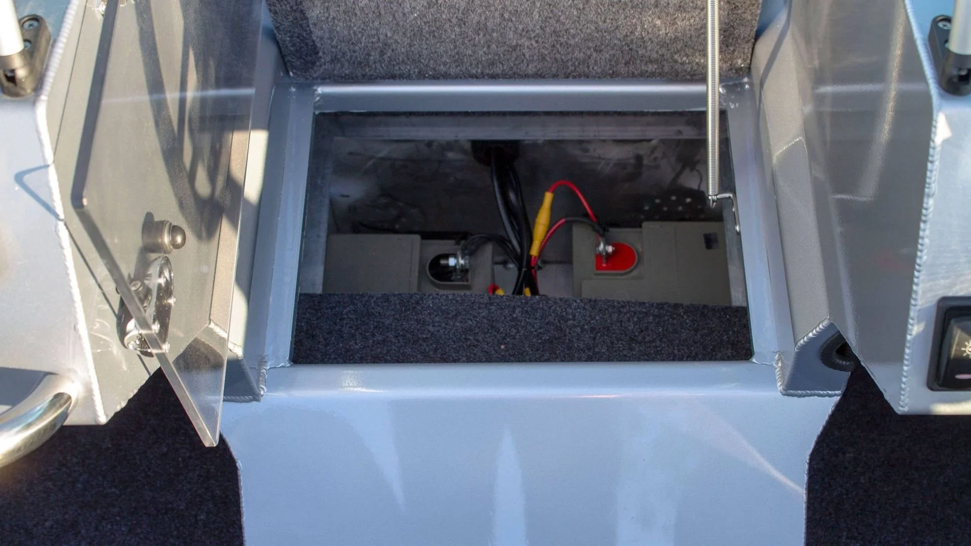 Open compartment with electrical wiring and batteries inside a vehicle.