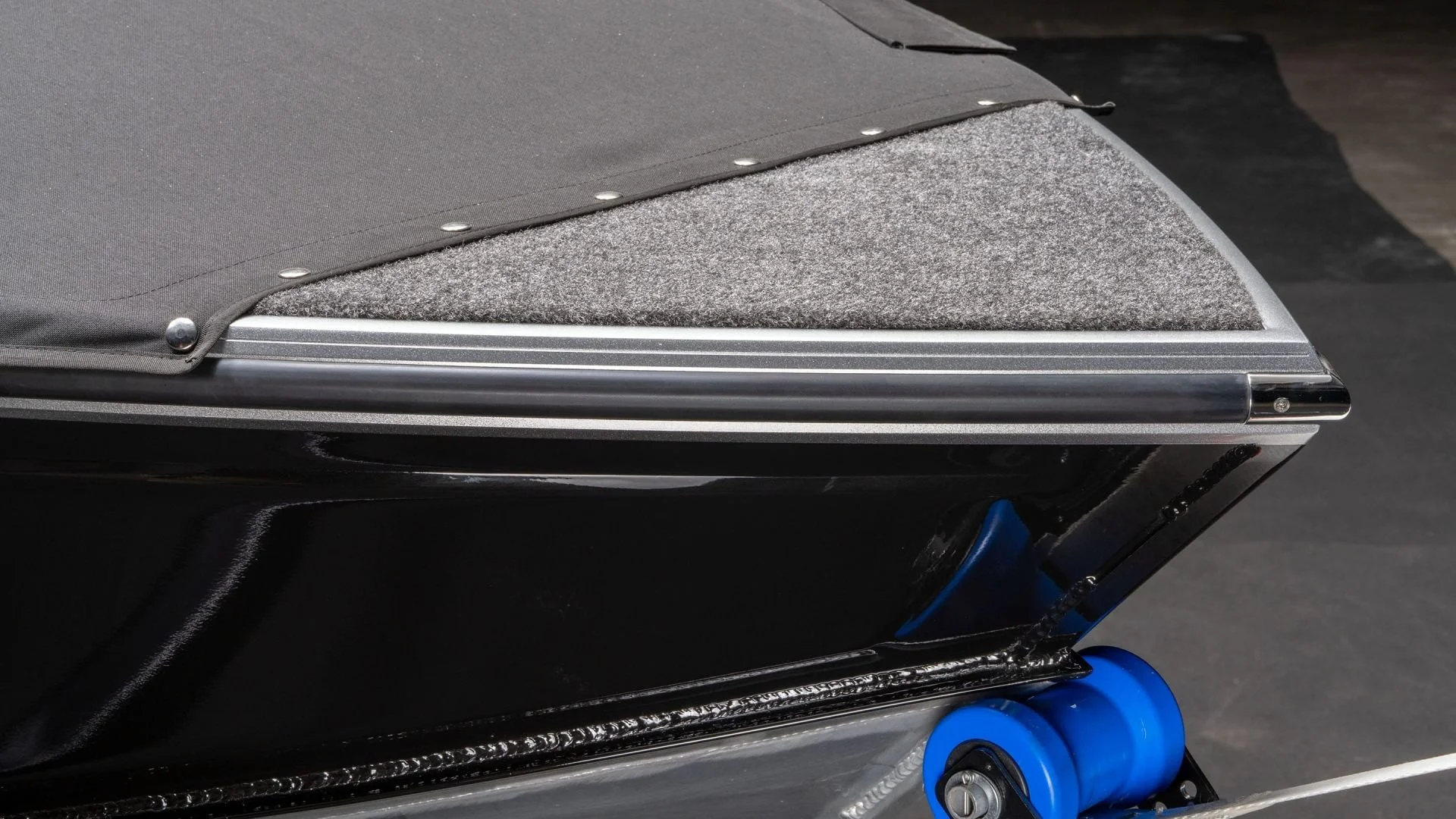 Close-up of a section of a skateboard or roller skateboard with black deck, gray grip tape, and bright blue wheels.