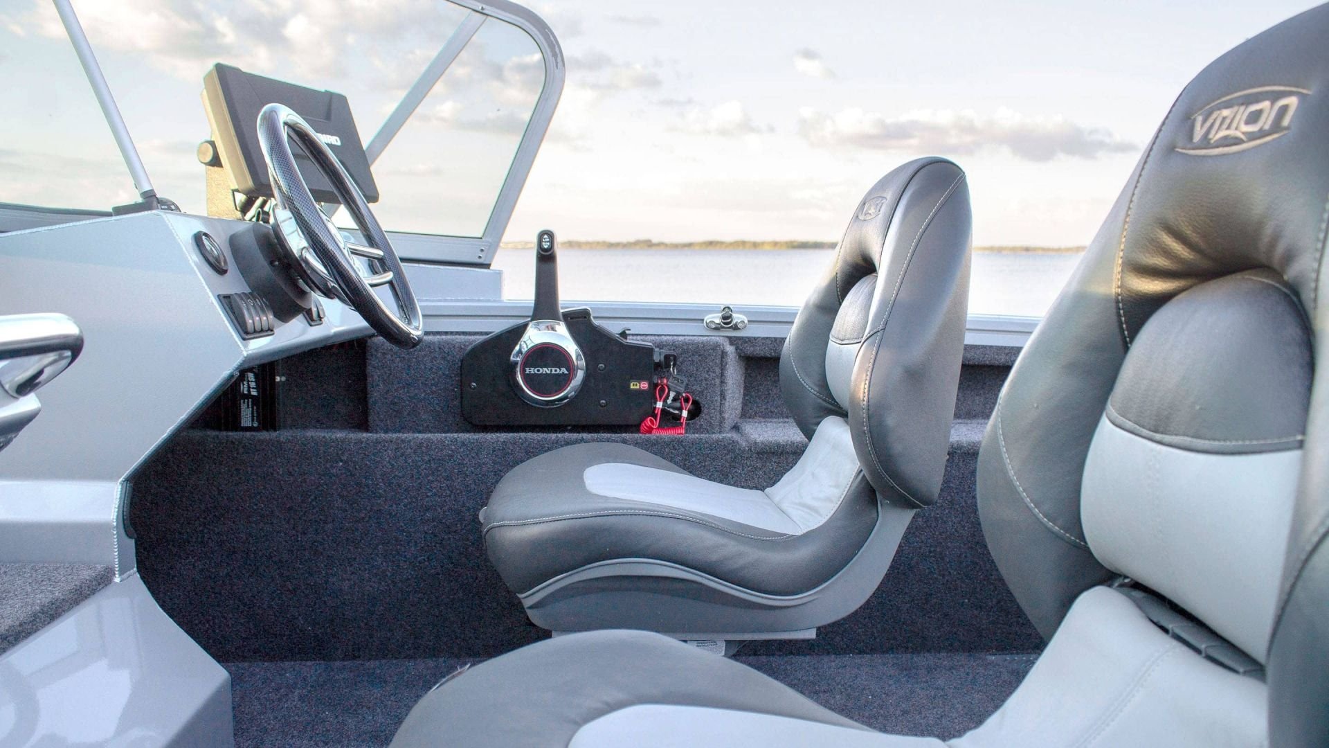 View of the interior of a boat, showing a captain's seat, passenger seats, a steering wheel, and navigation equipment, with water and sky visible through the windshield.