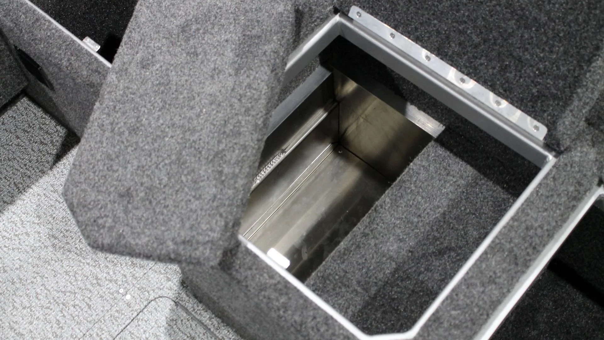Interior of a compartment in a vehicle with a metallic lining, surrounded by dark gray carpeted material.