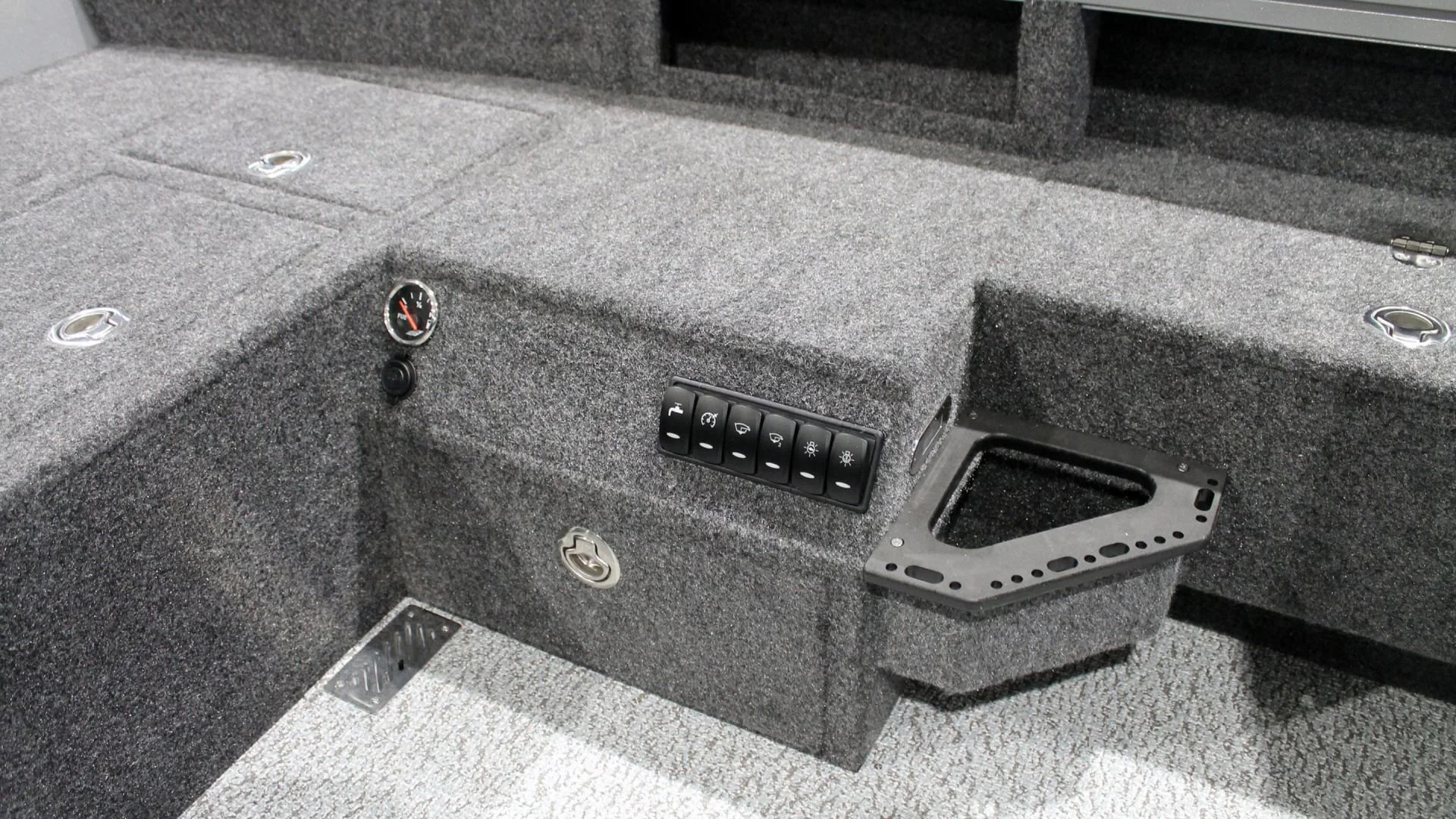 Close-up view of a grey textured surface with multiple control buttons, a small gauge, and mounting brackets, possibly part of a vehicle or equipment panel.