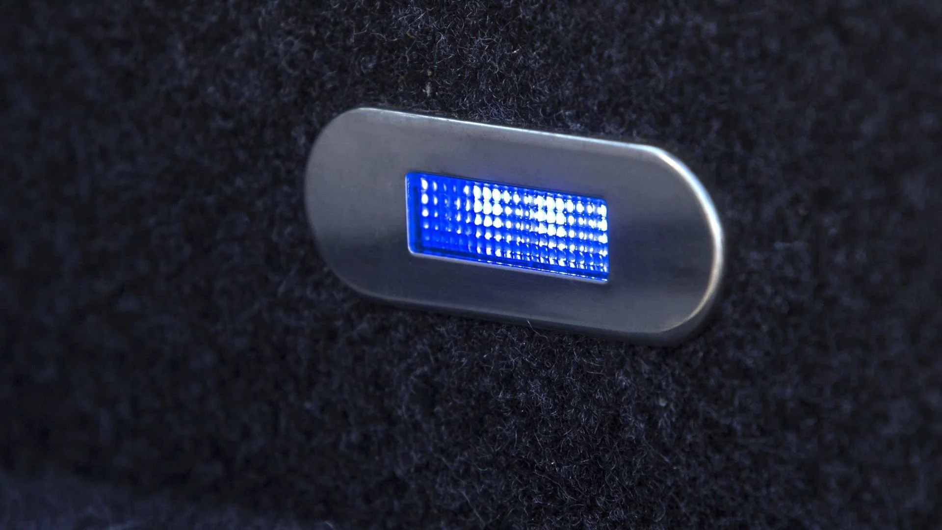 Close-up of a rectangular blue LED light embedded in black carpeted surface.