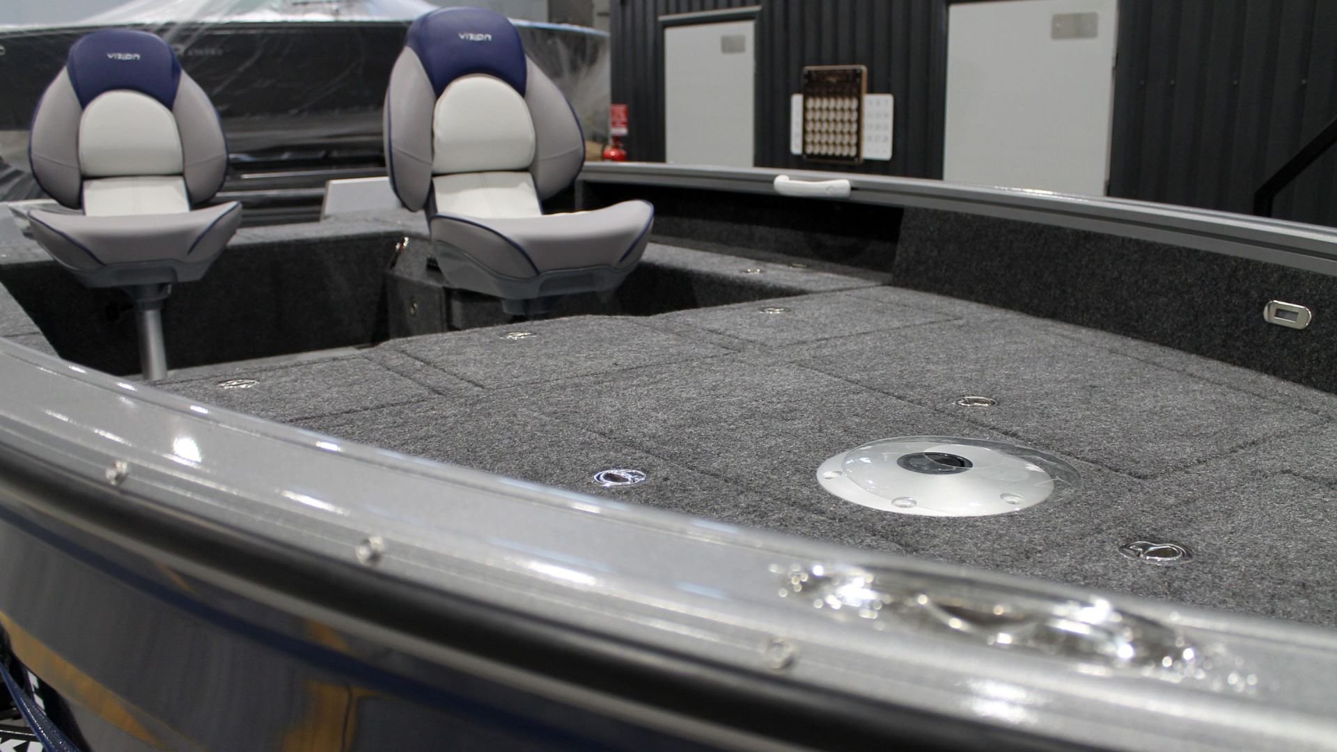 Interior of a boat with two gray and blue captain chairs, a carpeted deck, and various compartments.