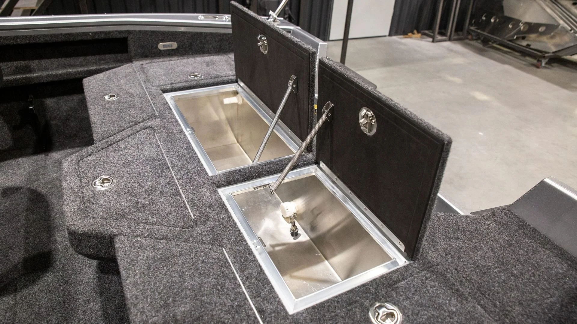 The image shows a boat's console with a constructed opening, featuring two rod holders and a storage compartment with a metal interior. The surrounding surface is covered with dark, textured material.