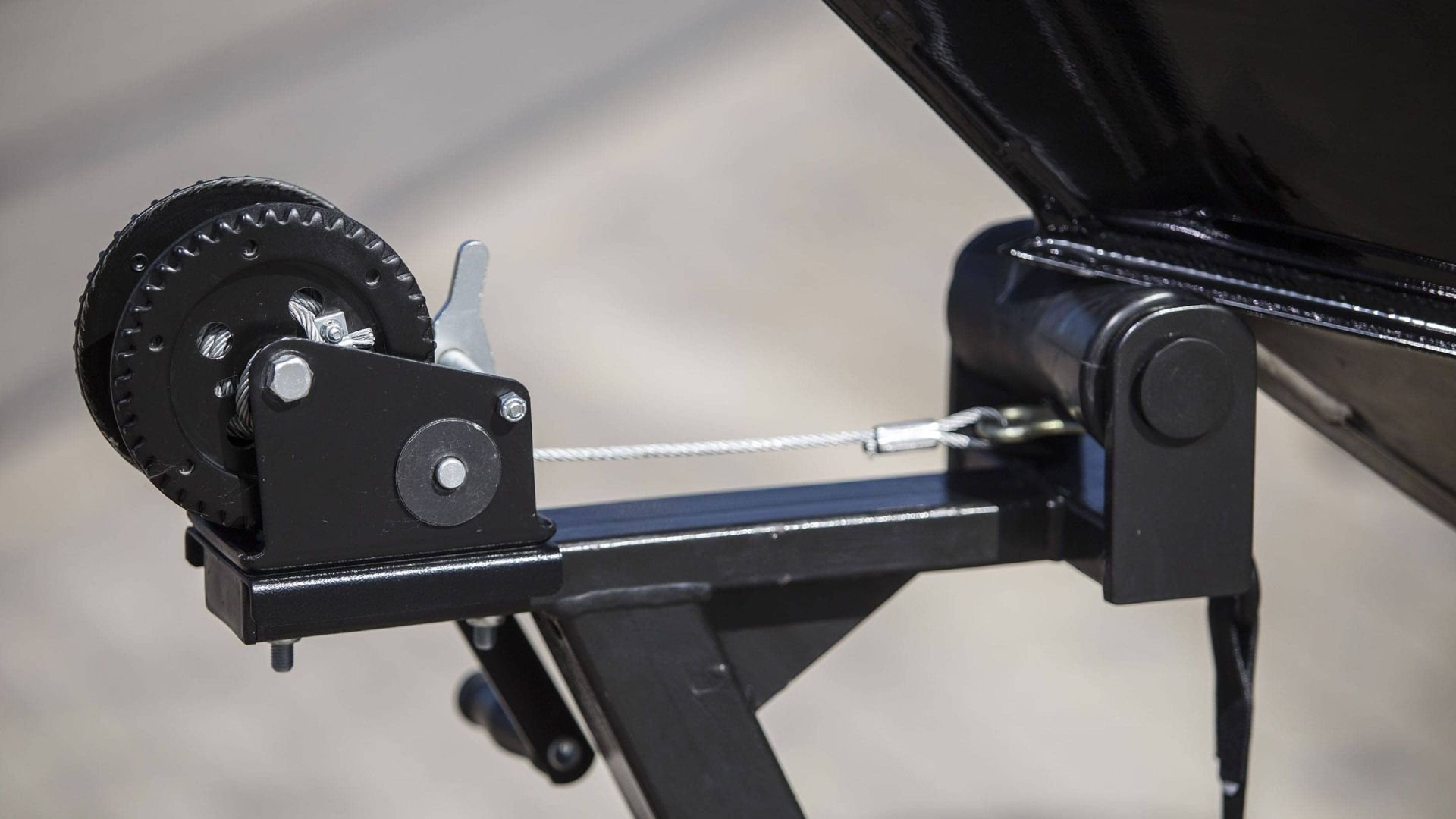 Close-up of a black boat trailer winch with a wheel, hook, and cable, mounted on a black metal frame.