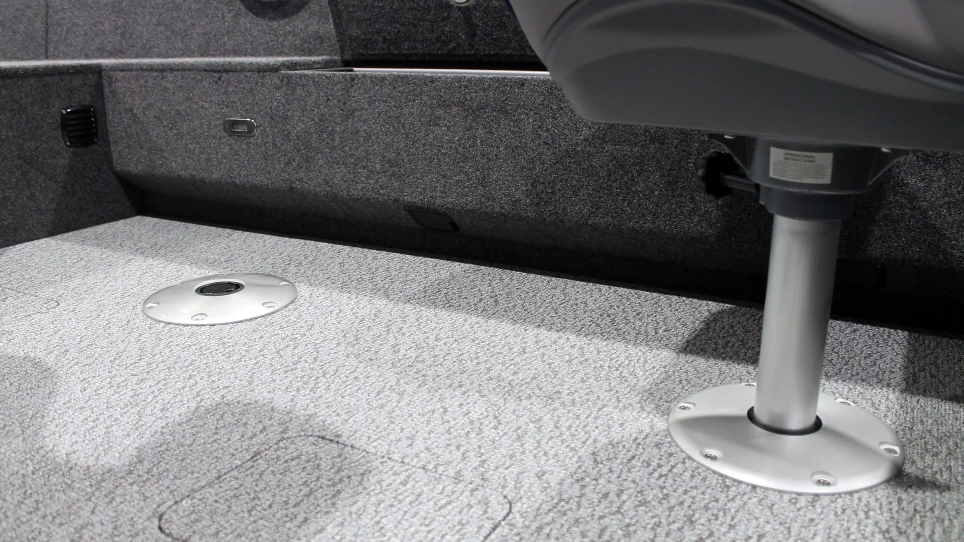 The image shows the interior of a vehicle with grey speckled flooring, a metal mounting plate on the floor, and a support pole attached to the floor with a round base.