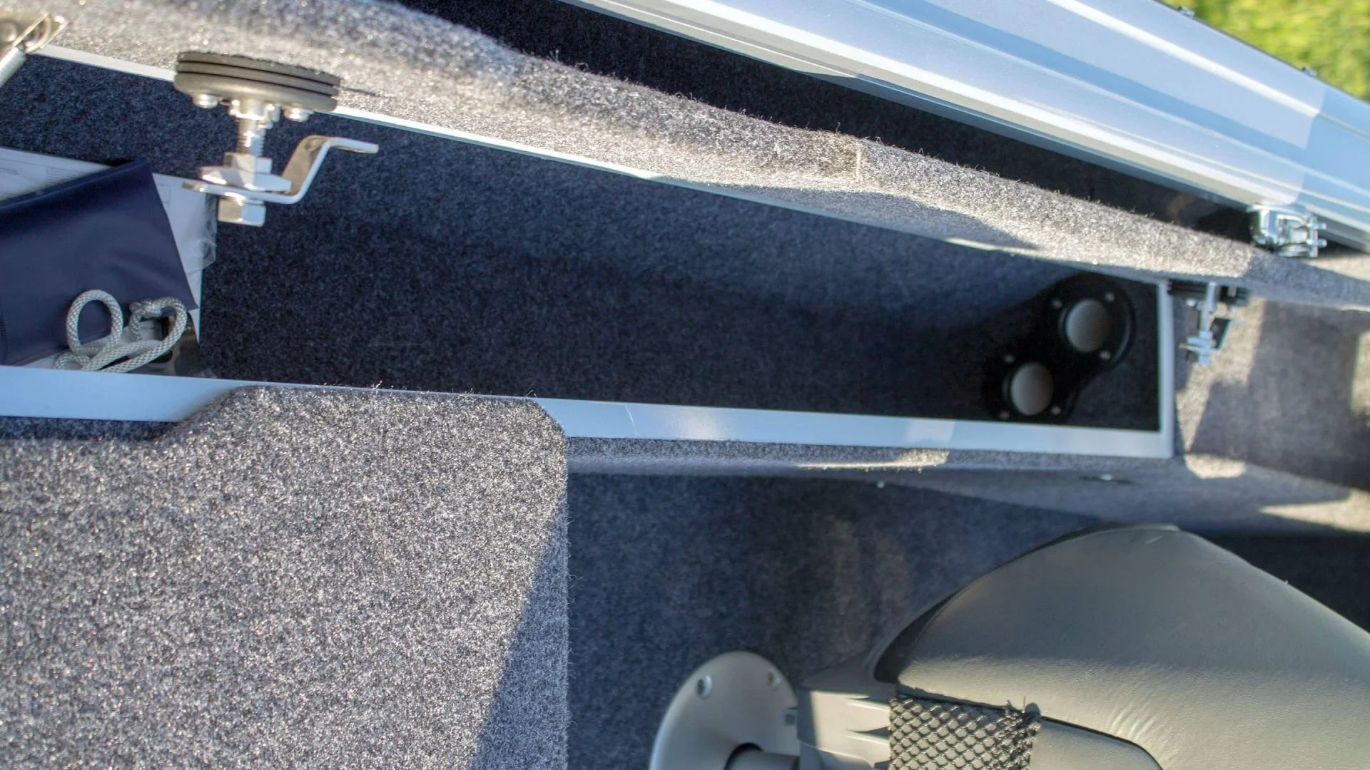 Close-up view of the interior of a boat, showing speaker mounts, foam padding, and a section of grey carpeting.