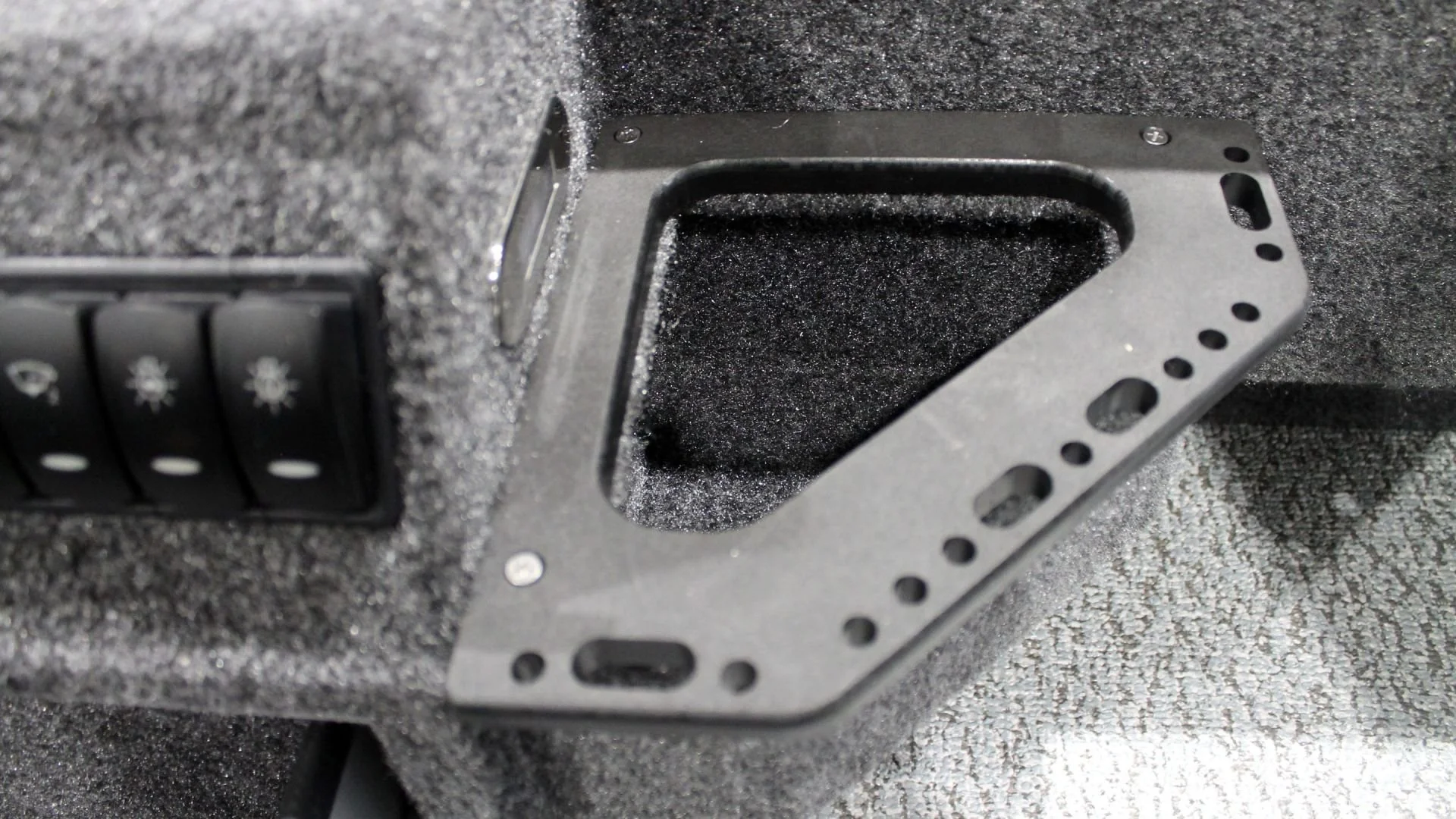 Close-up view of a black rectangular speaker enclosure with foam interior, mounted on gray textured surface, with a black panel featuring three switches.