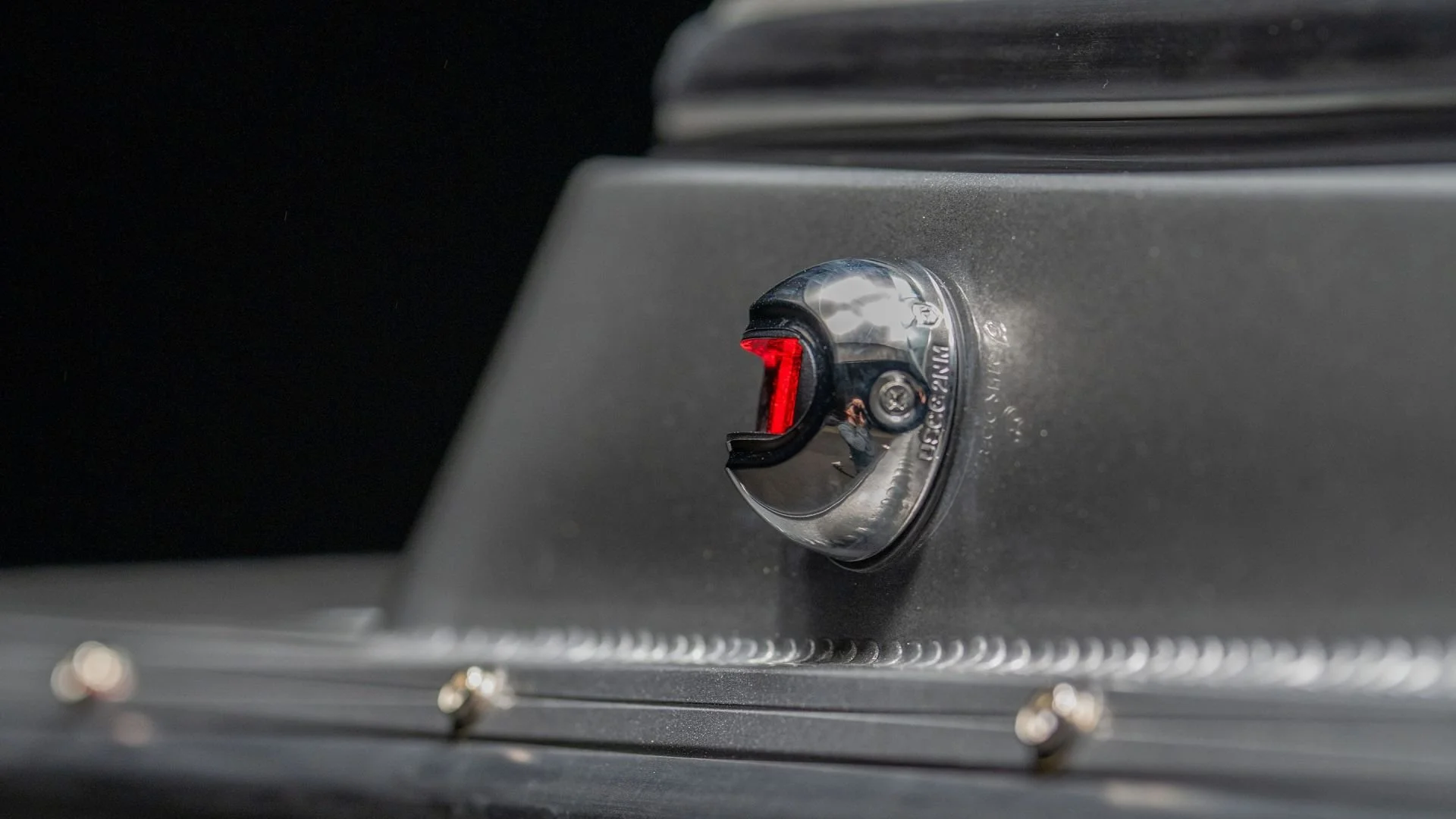 Close-up of a toggle switch with a red indicator light, mounted on a metallic surface, part of a machine or control panel.