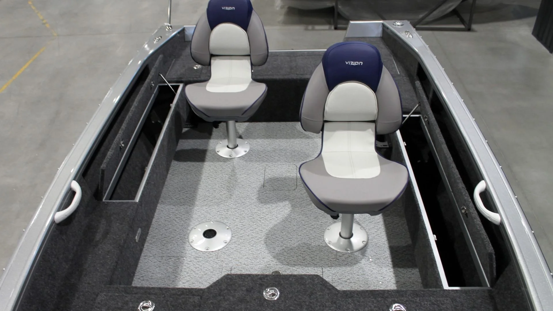 Two gray and navy blue Vizon boat seats on a boat deck, with storage compartments on the sides and a carpeted floor.