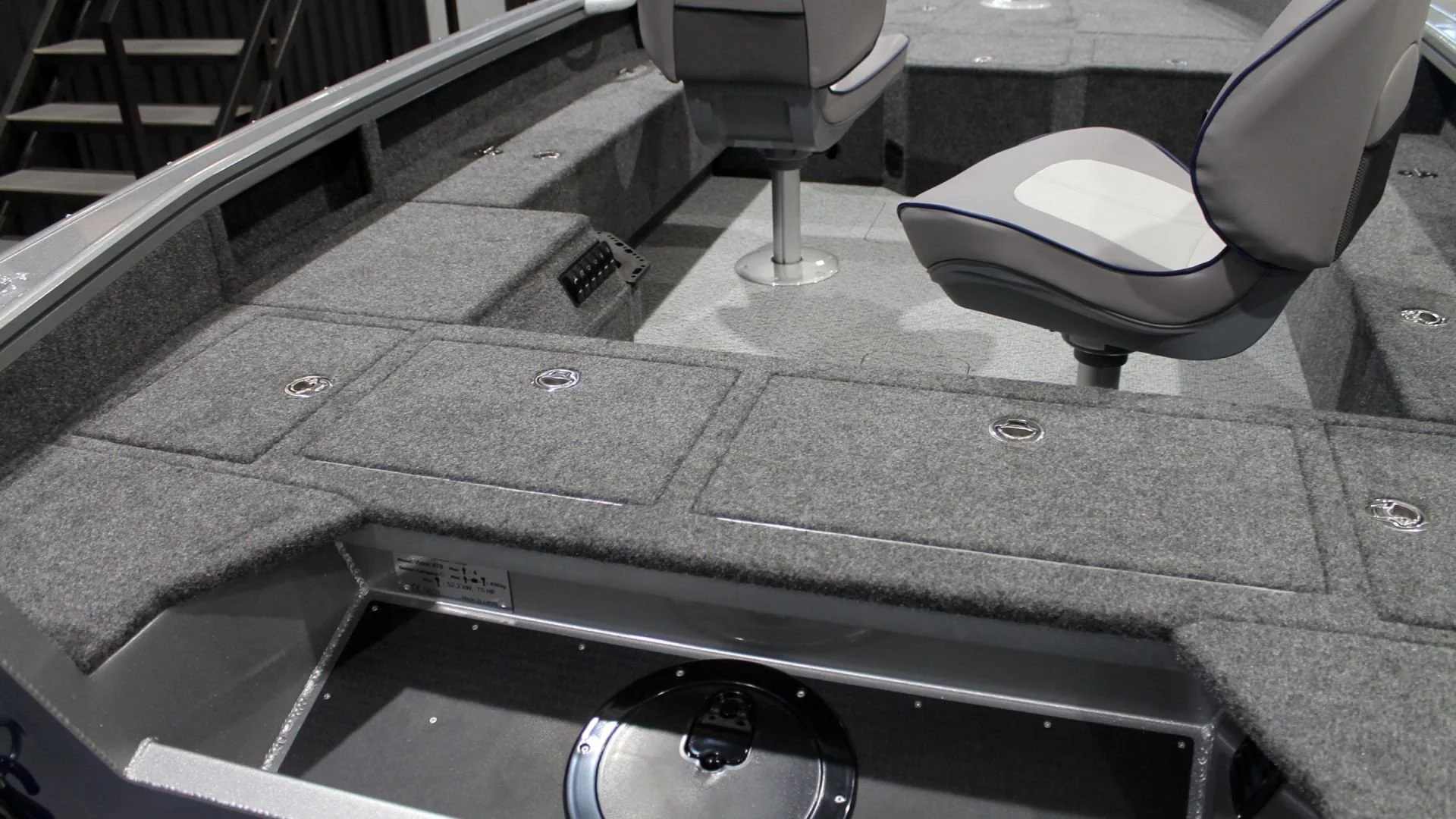 The interior of a fishing boat with gray carpeted floor, two gray swivel seats, and built-in storage compartments.