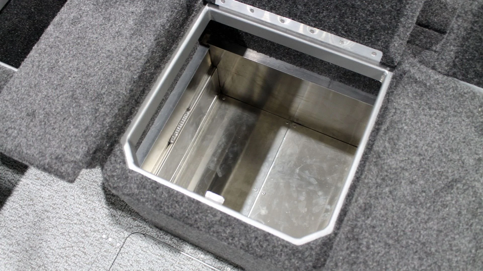 Empty embedded compartment inside a built-in countertop, likely in a kitchen or office setting, surrounded by gray fabric or carpeting.