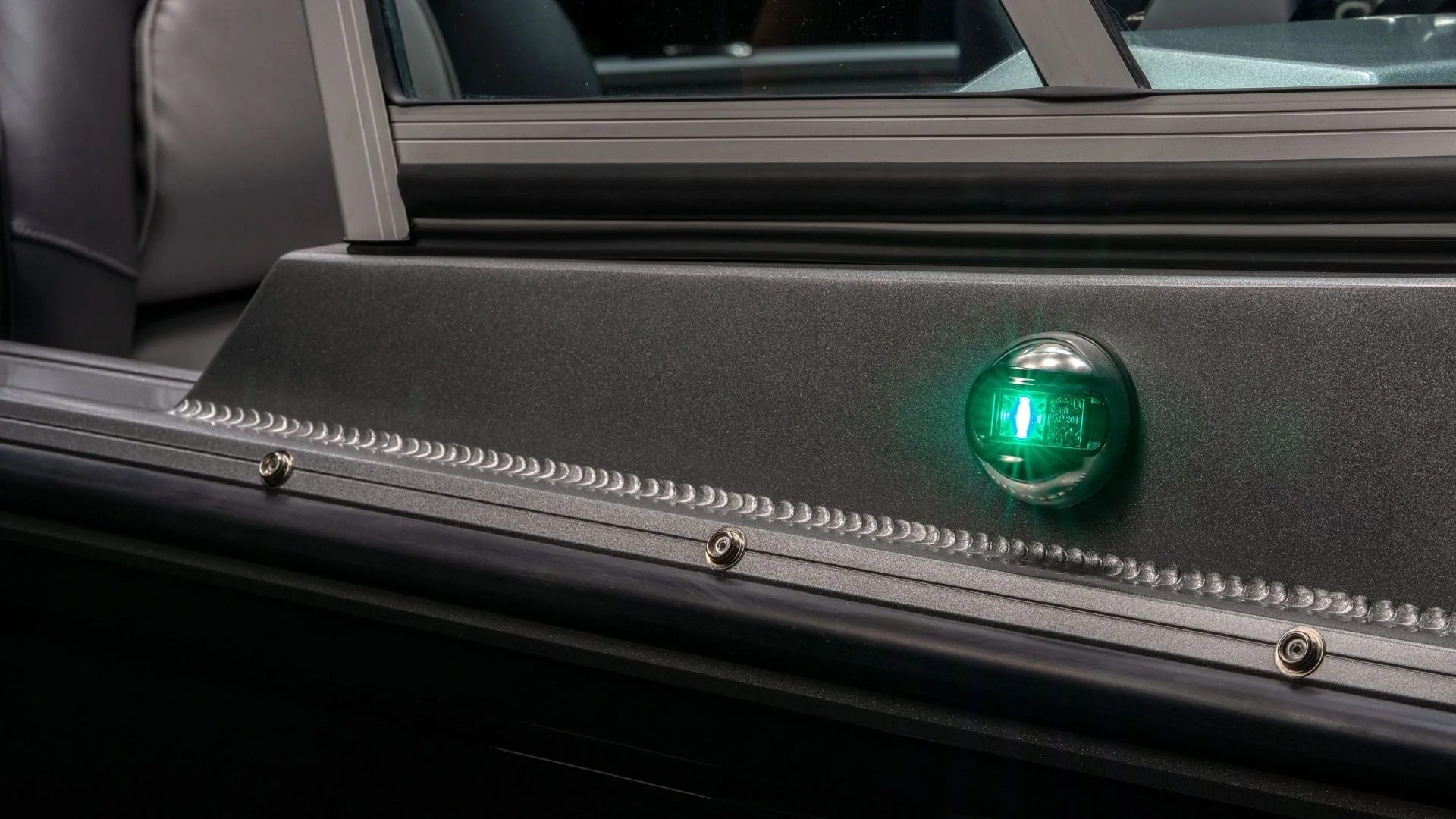 Close-up of a metallic surface with screws and a green-lit sensor or indicator light, part of an electronic or mechanical device.