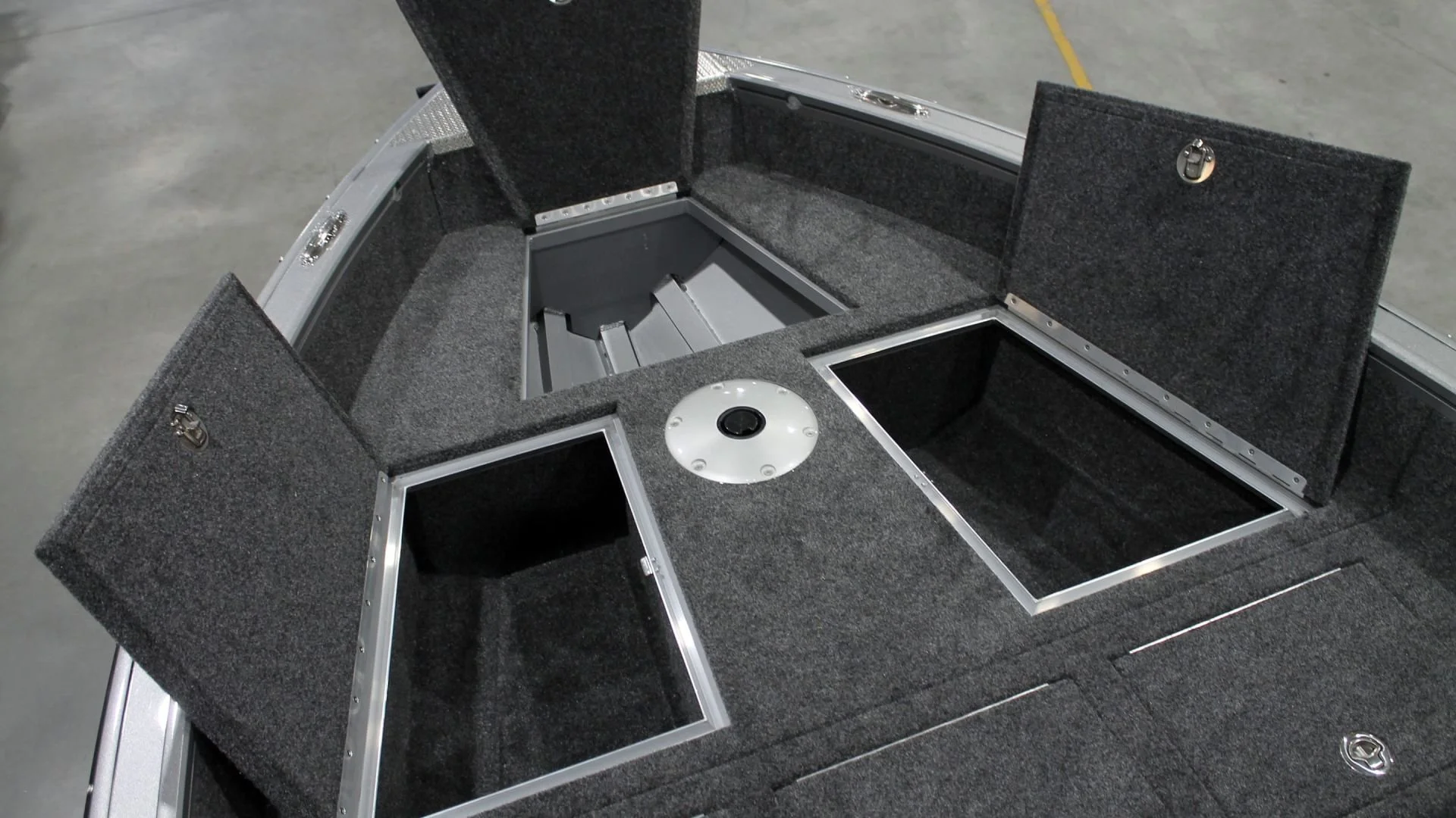 The interior of a boat compartment with open storage compartments, a round mount in the center, and carpeted surfaces.