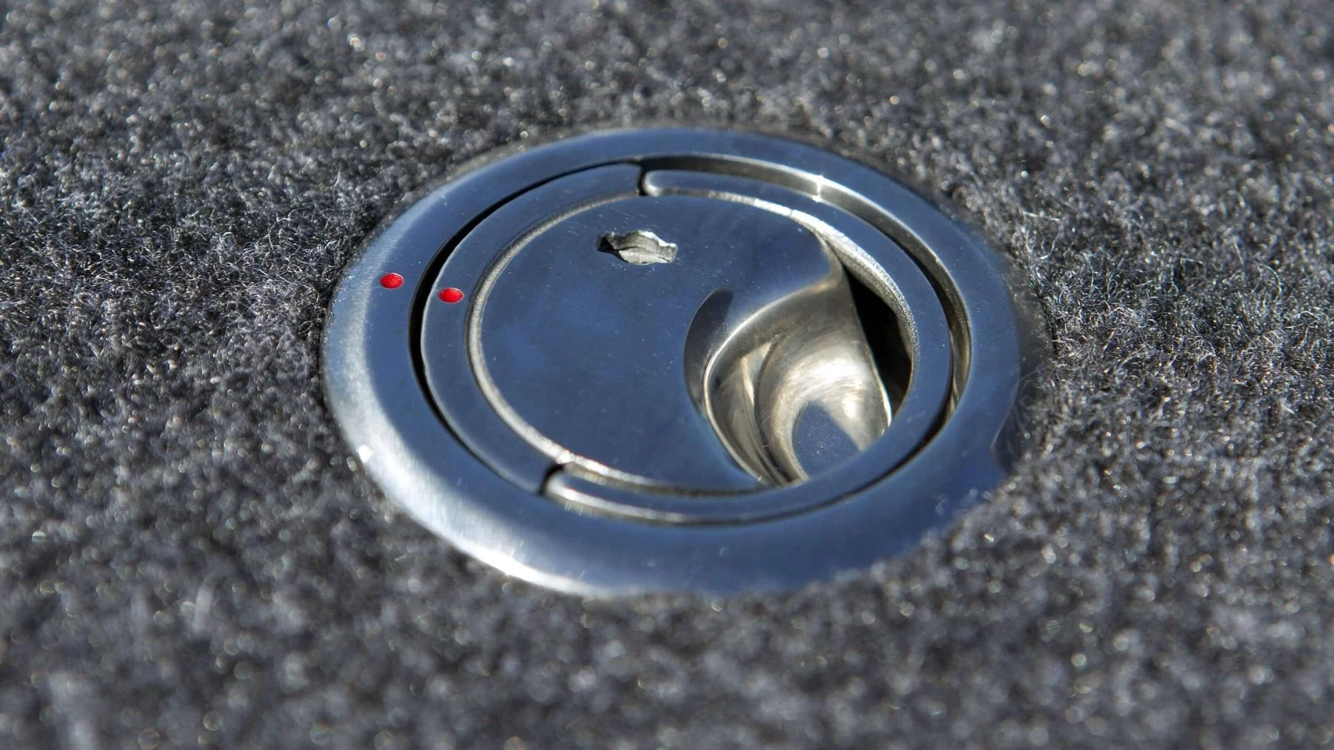 Close-up of a metallic car fuel cap on a black textured surface.
