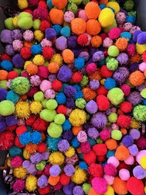 A pile of pom-poms in assorted colors such as yellow, green, pink, blue, purple, and red.