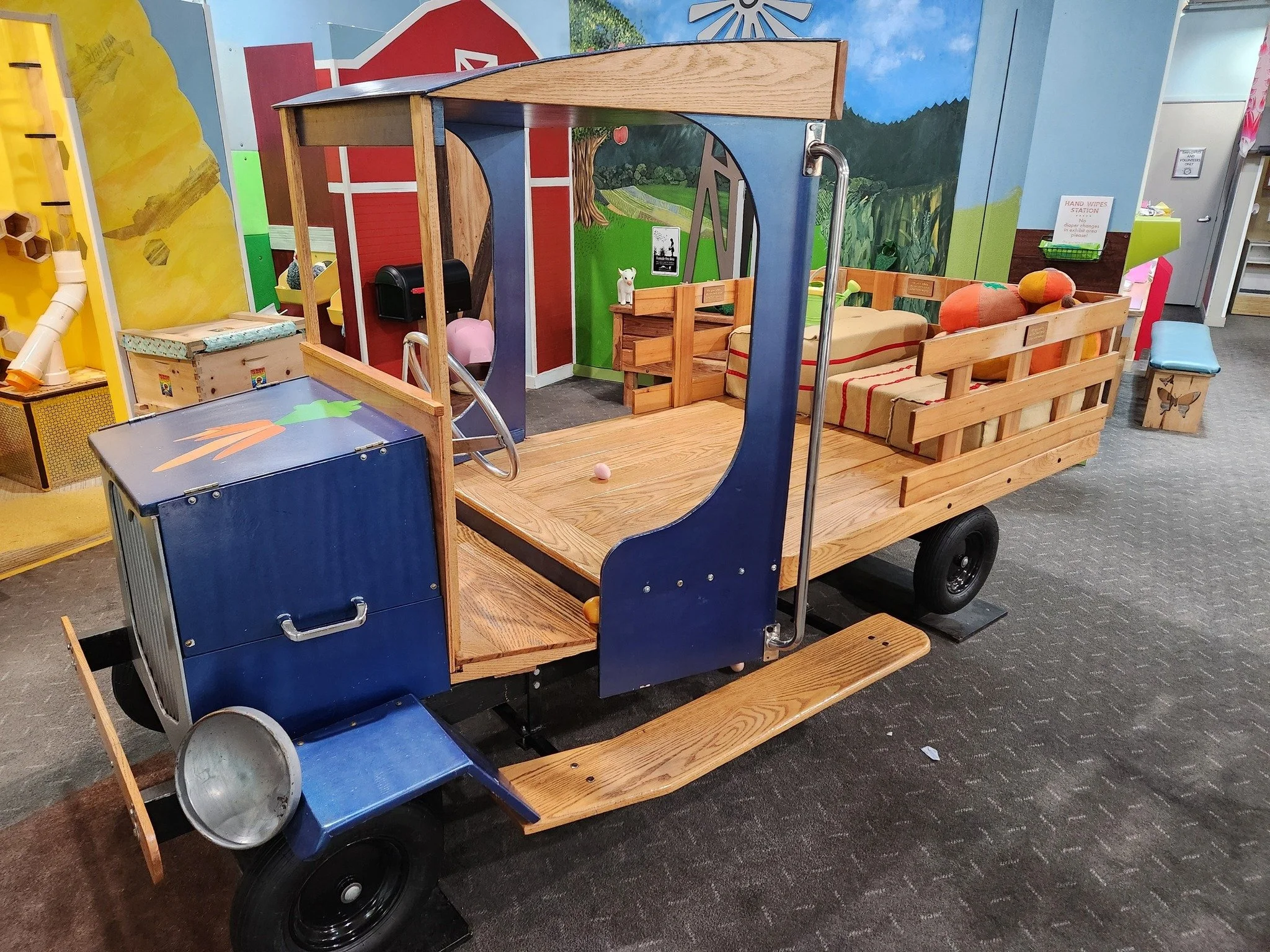 A wooden farm truck that was once a twin-sized bed for a child. The truck has two steps leading into the bed of the truck, a steering wheel, hay bales, pumpkins, and a roof covering the driver's seat. 