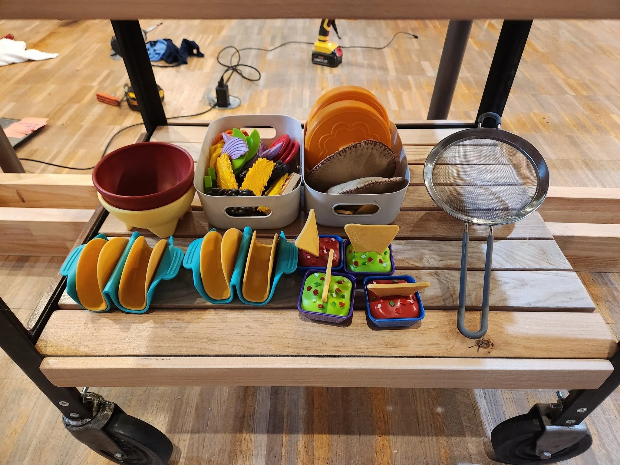 A shelf displaying pretend ingredients and utensils to make tacos and chips and salsa.