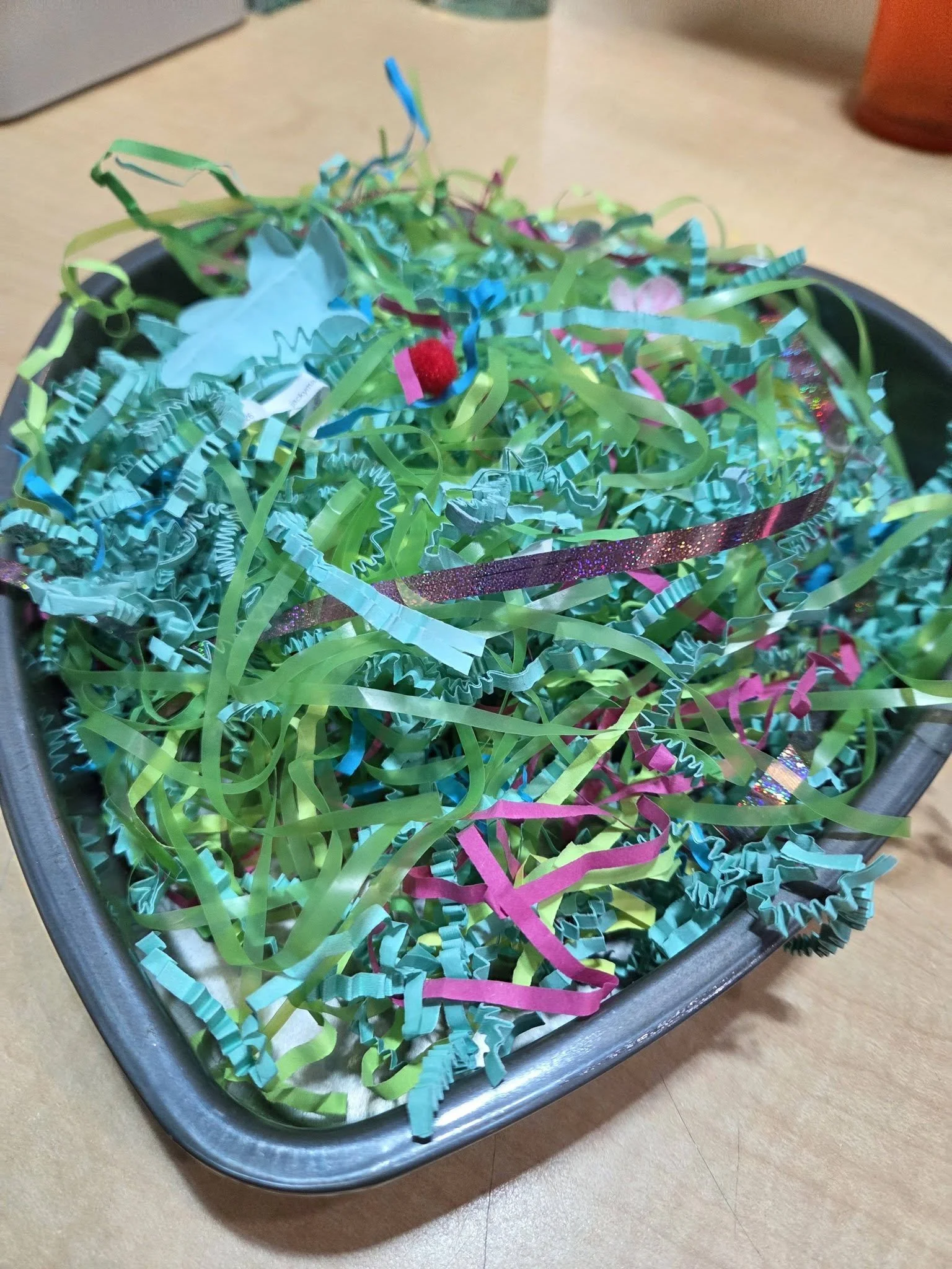 A heart-shaped pie tin with colorful shredded paper inside. 
