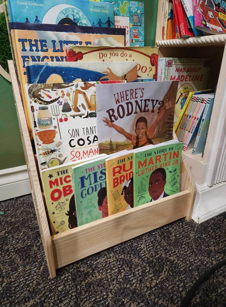 Wooden book display featuring various books such as "Martin Luther King, Jr." and "Where's Rodney?"