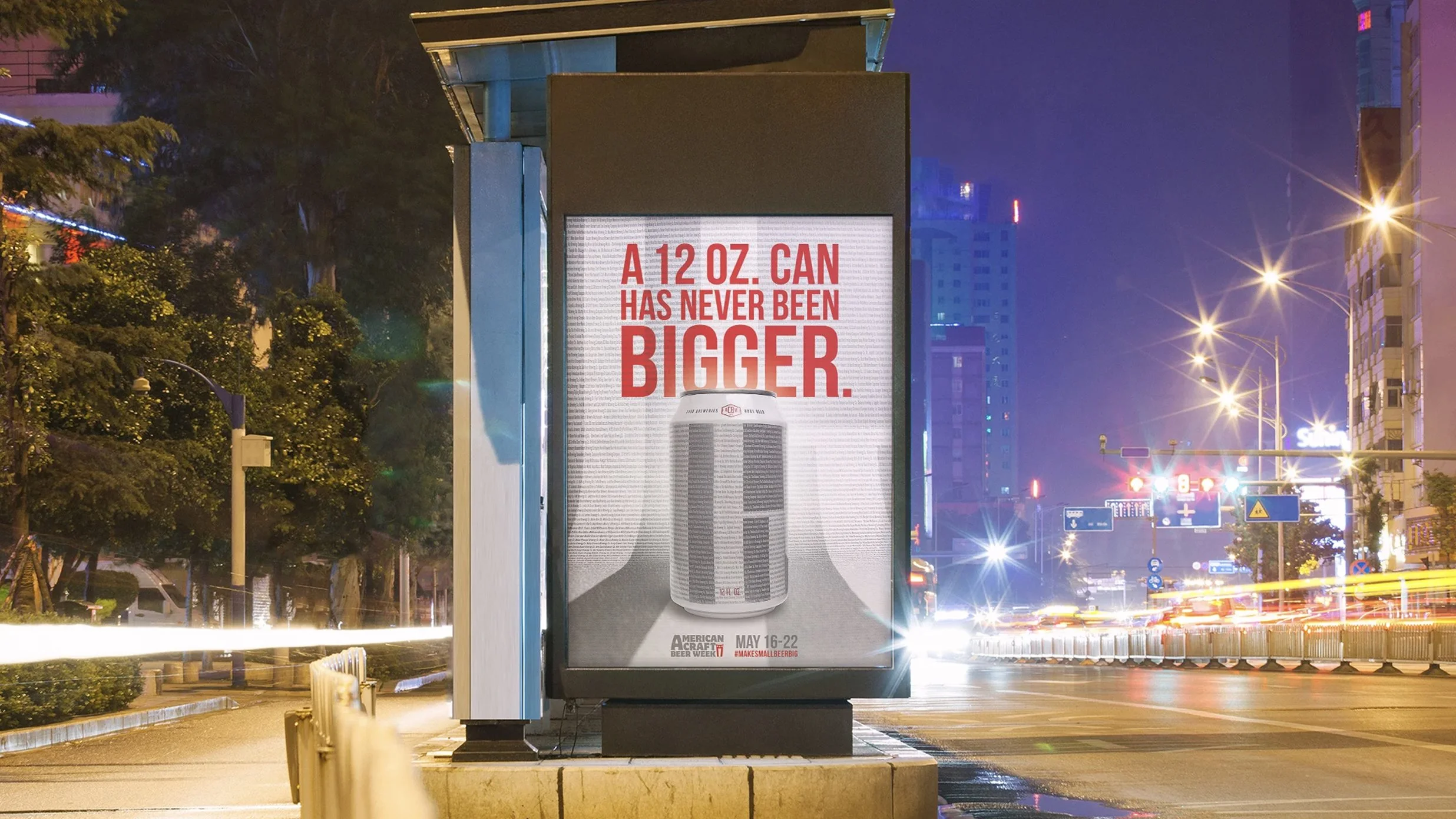 An outdoor billboard advertising a 12 oz. beer can, with the text 'A 12 oz. can has never been bigger,' on a city street at night. The street is illuminated by streetlights, with moving car lights creating streaks of light.