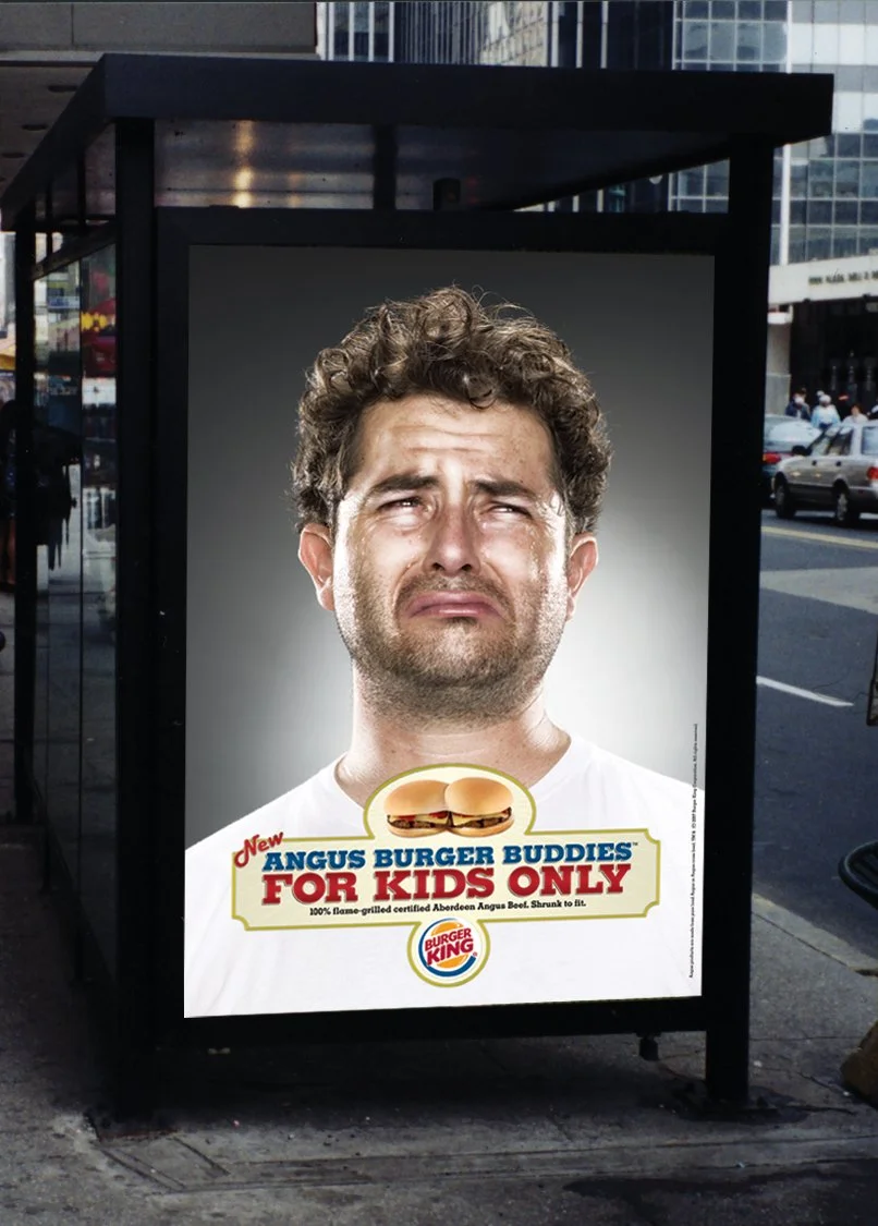 A billboard ad for Burger King features a man with a distressed expression and a large double cheeseburger graphic. The text reads 'New Angus Burger Buddies for Kids Only' with a note about a certified Angus beef patty.