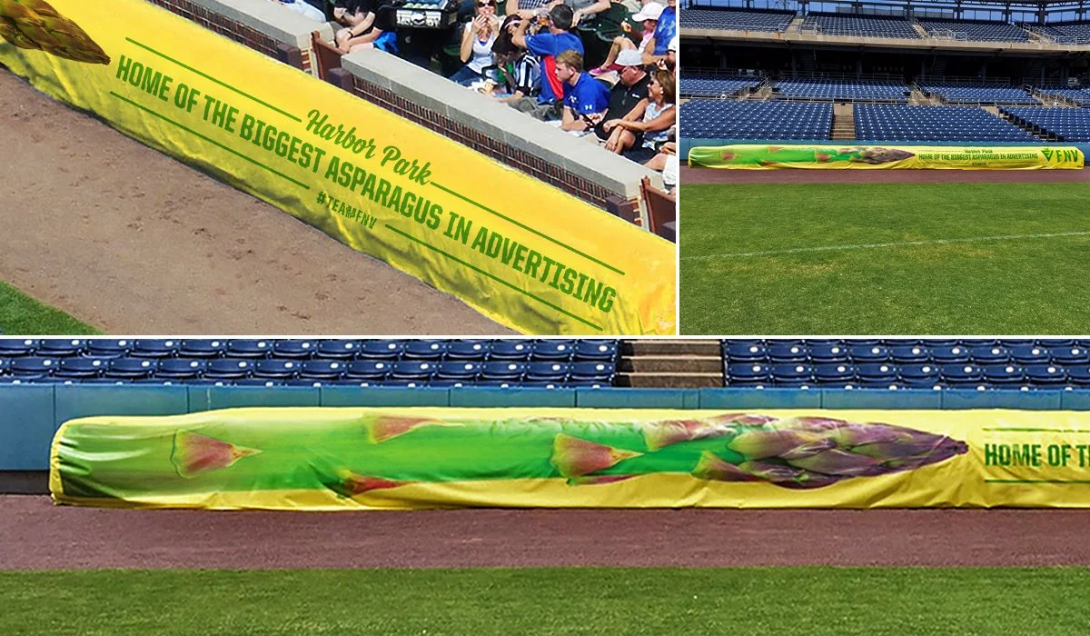 Promotional vinyl banner advertising the asparagus capital of the world at Harbor Park stadium, with spectators in the background.