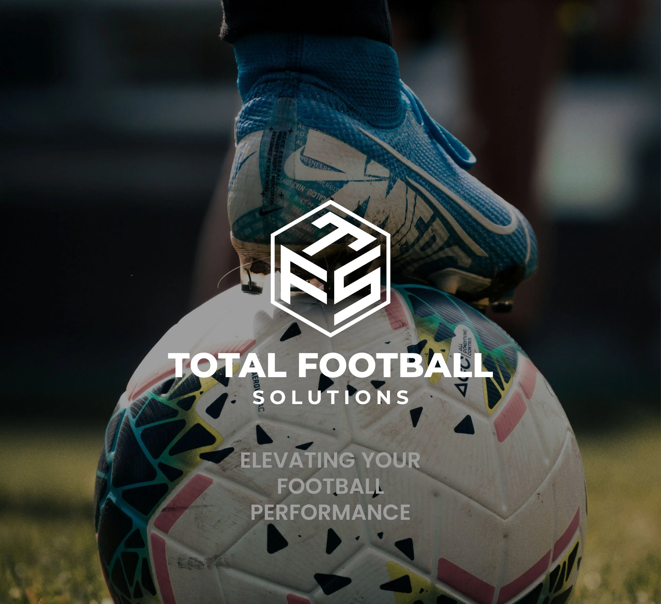 A close-up of a footballer's foot wearing a blue cleat, balancing on top of a soccer ball on a grassy field, with overlaid logo and text for Total Football Solutions.