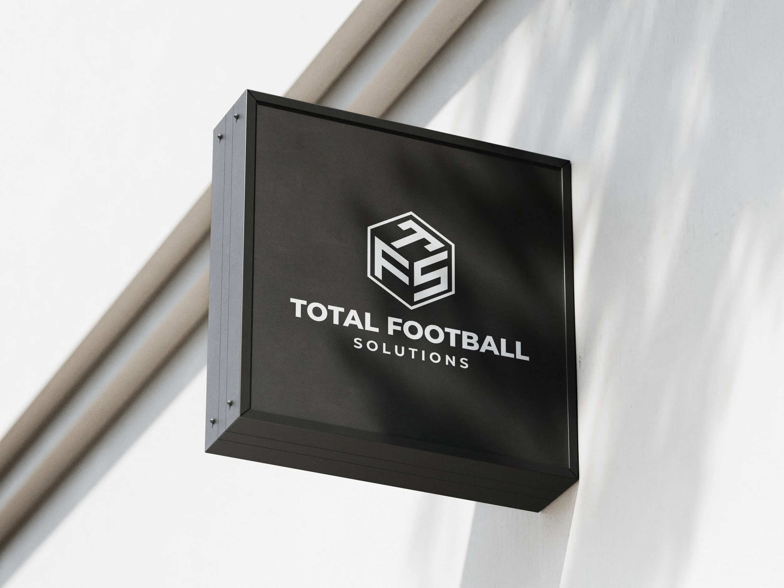 Black sign with white logo and text for Total Football Solutions mounted on a white wall.