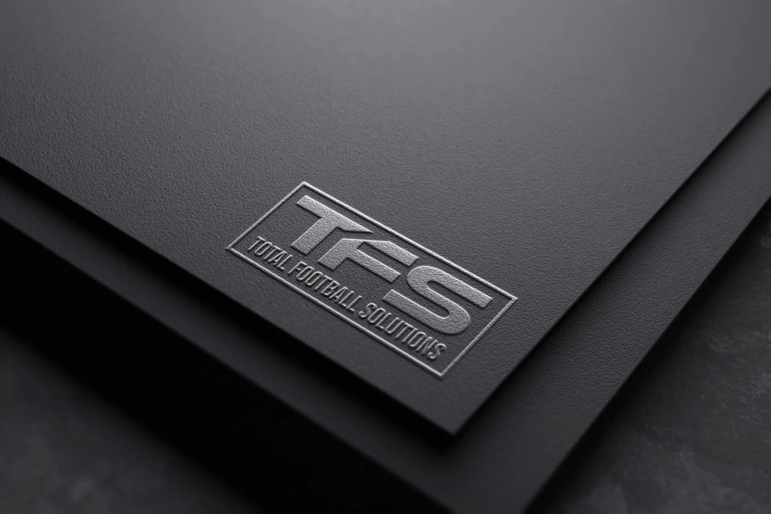 Close-up of black textured surface with embossed 'TOTAL FOOTBALL SOLUTIONS' logo.