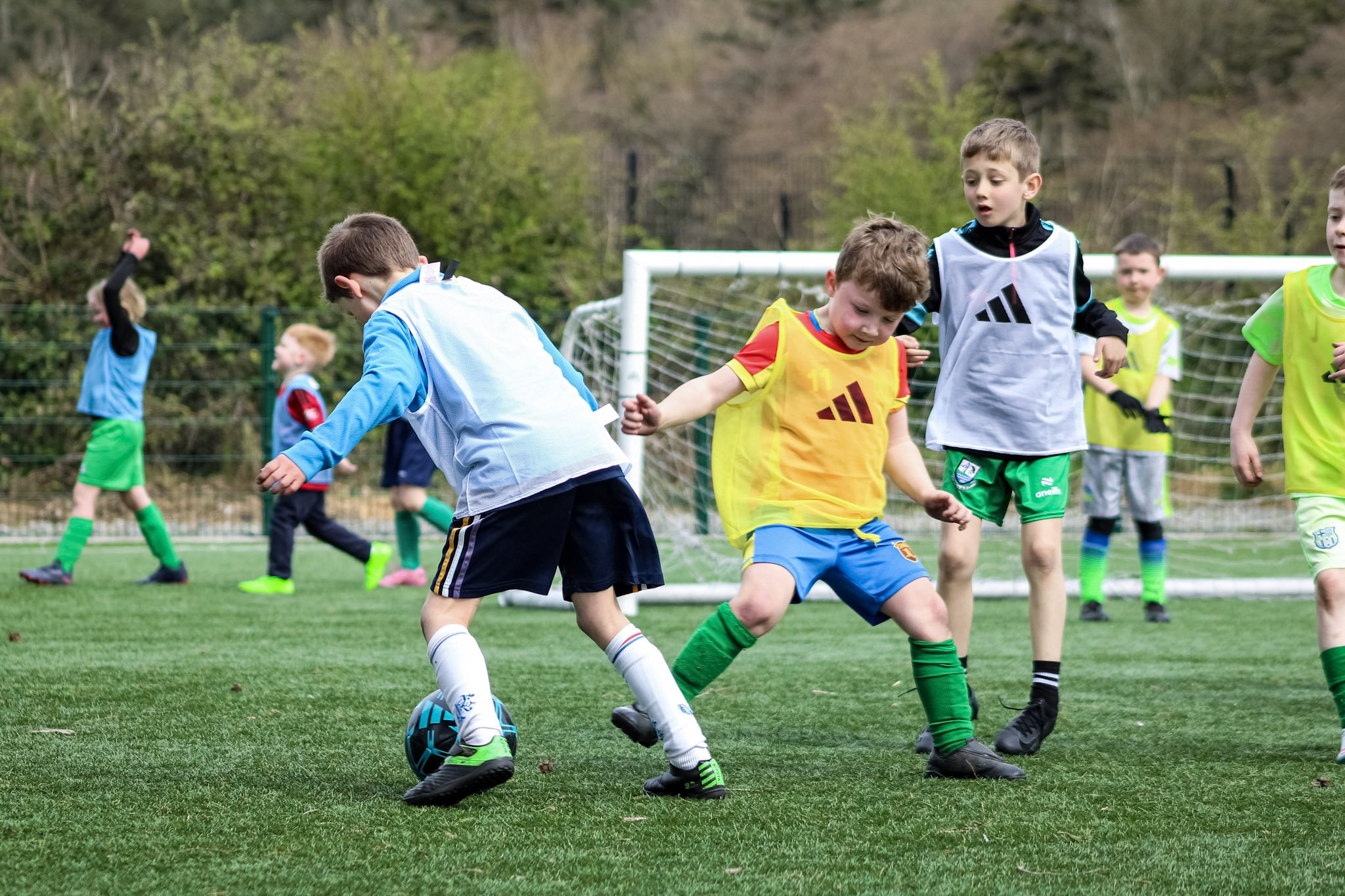 Children playing soccer on a field, with some kids wearing vests and others in jerseys, actively competing for the ball.