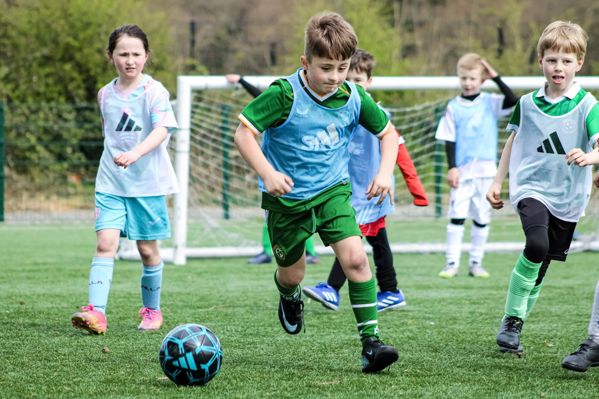 Kids playing soccer on a grassy field with goalposts in the background.