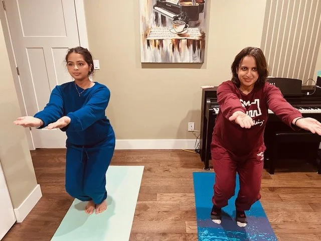 WhiteFlutter founder and student practicing yoga Chair Pose (Utkatasana) in a curated home sanctuary, featuring professional mats and a large-scale piano canvas visual anchor to support nervous system regulation.