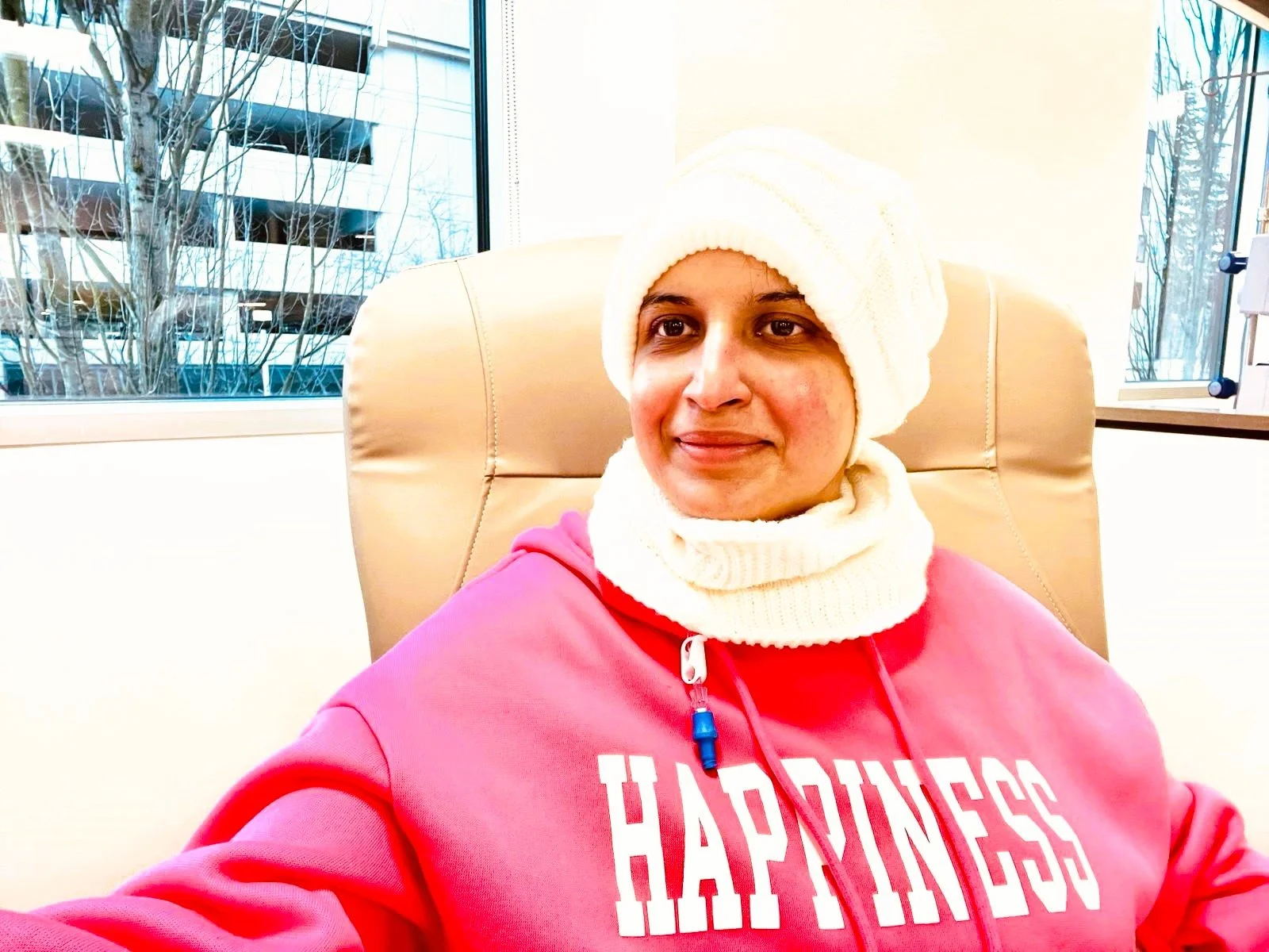 WhiteFlutter founder Gauri during breast cancer treatment, wearing a pink "HAPPINESS" sweatshirt and white knit headwear, symbolizing the personal resilience and journey from recovery to expansive joy