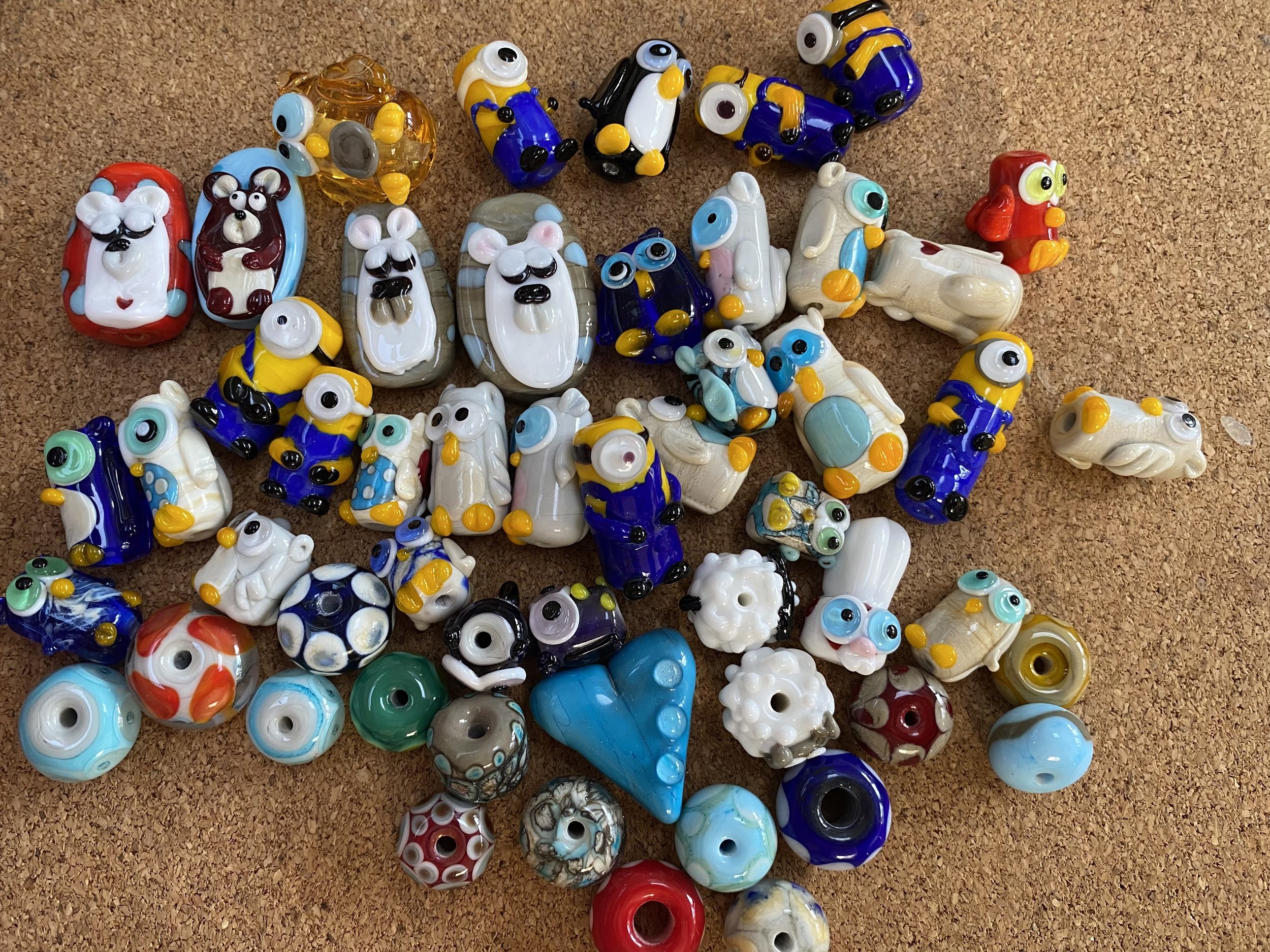 A collection of colorful glass beads and small glass figurines arranged on a cork surface.