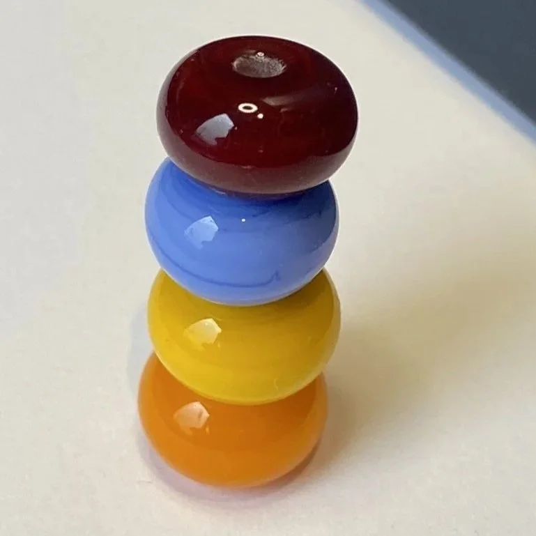 Stacked beads in red, blue, yellow, and orange colors on a white surface.