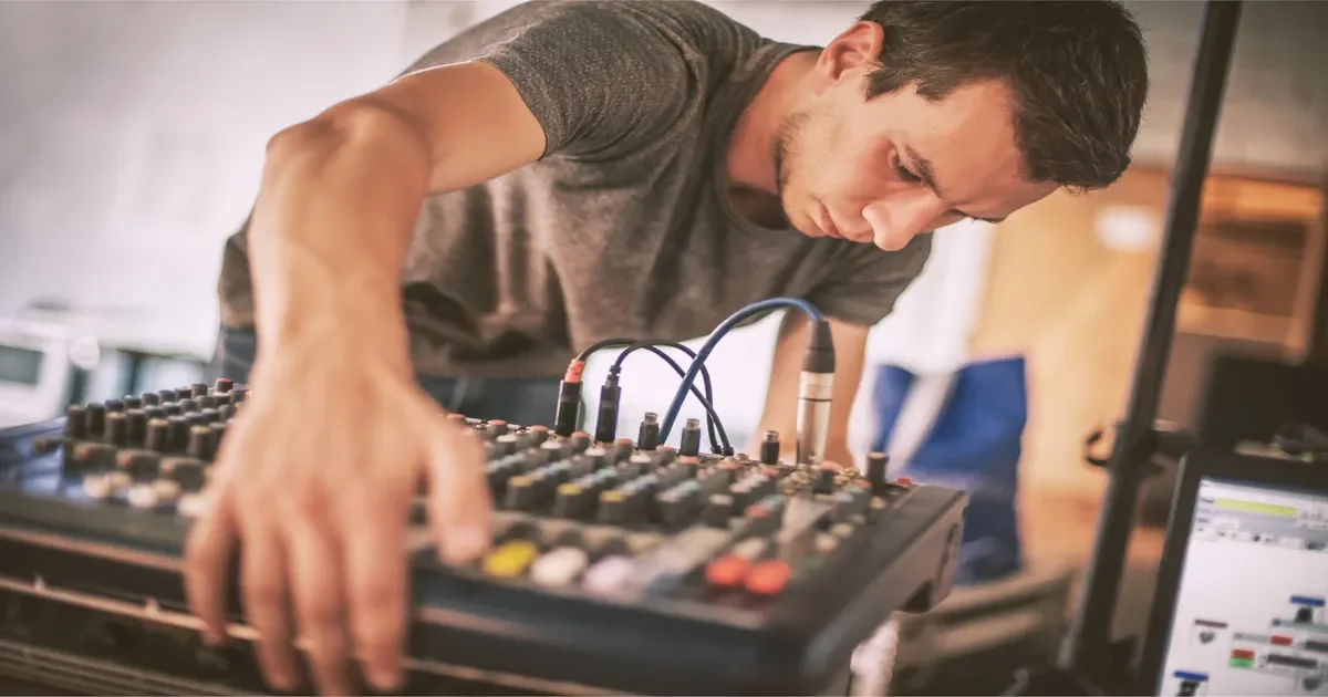 A man adjusting audio equipment with knobs and cables, possibly a DJ or music producer.