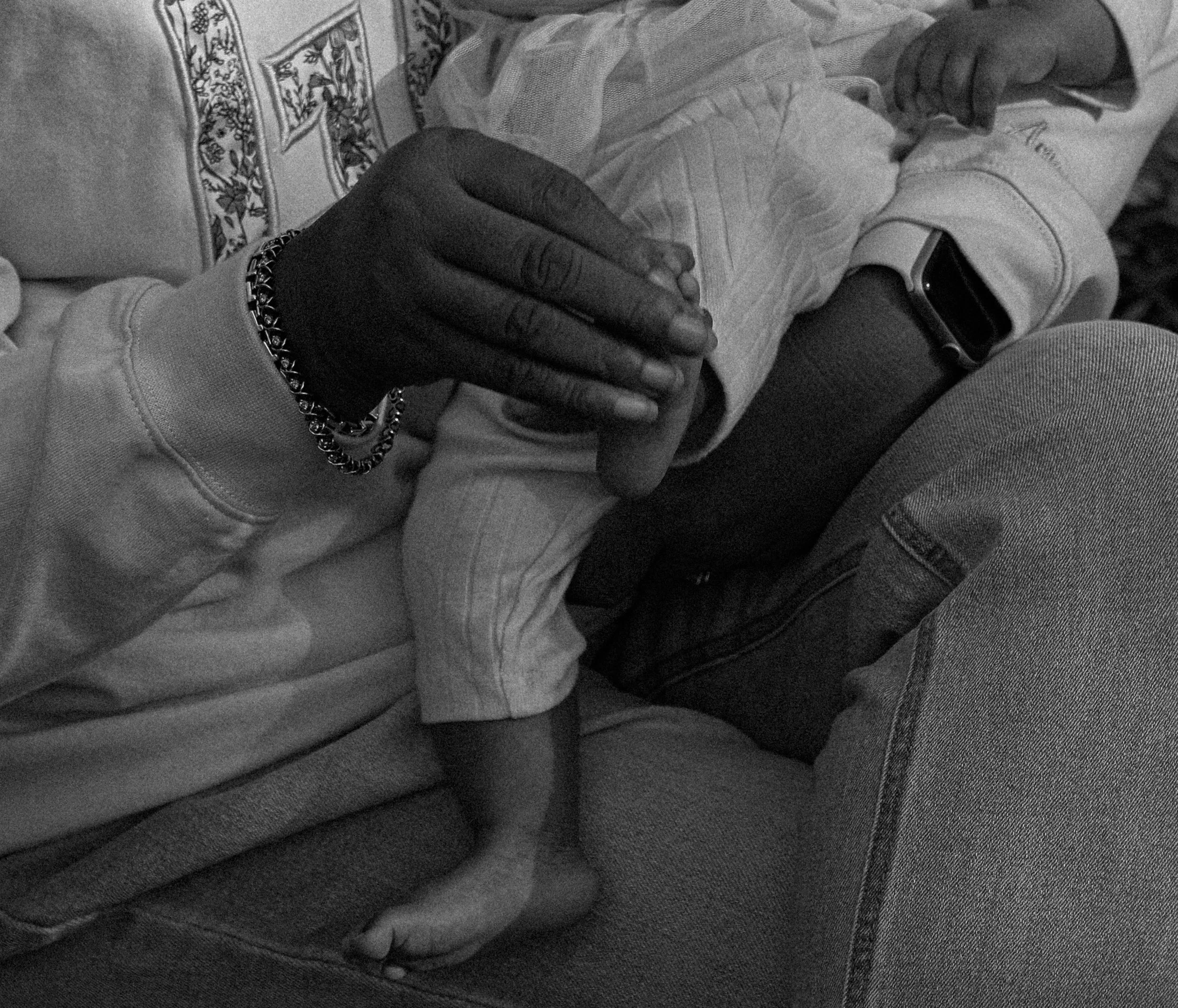 Two people sitting close together, with one person's hand resting on the other's arm, wearing a bracelet and a ring, both dressed casually.