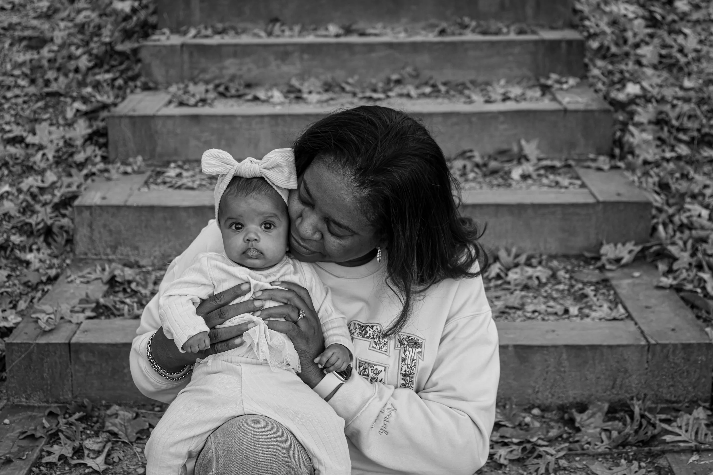A woman holding a young girl on her lap outdoors on a staircase with fallen leaves.