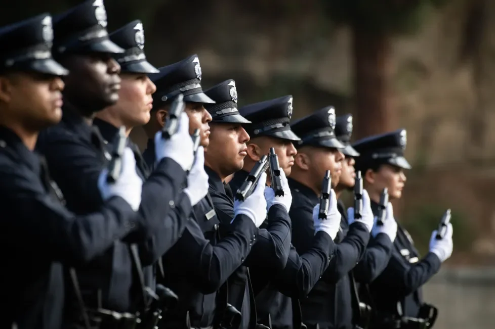 Line of police officers in uniform holding guns during a ceremony.