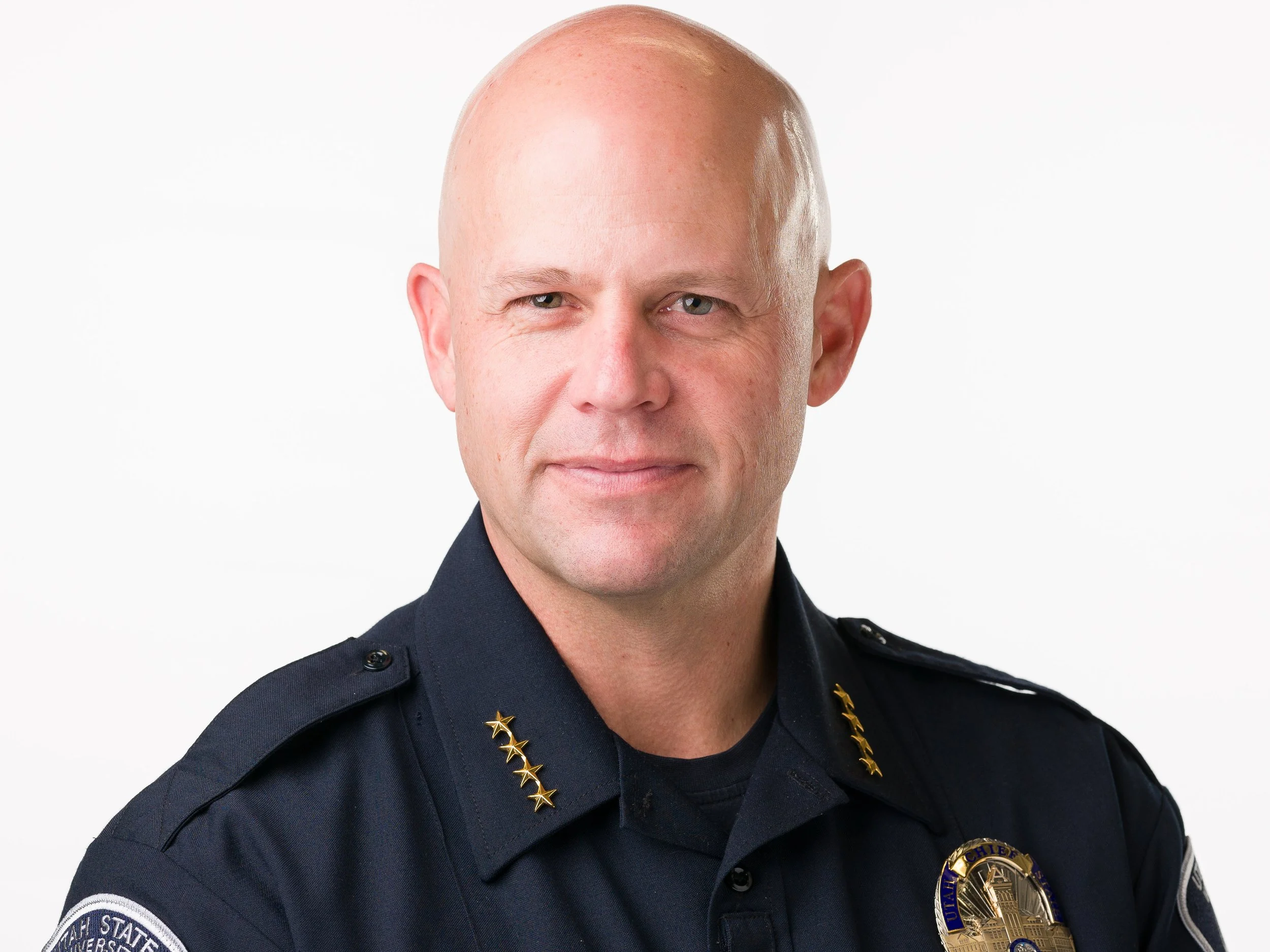 Portrait of Chief Blair Barfuss in a police uniform wearing a gold badge and a gold star chain, standing against a plain white background.