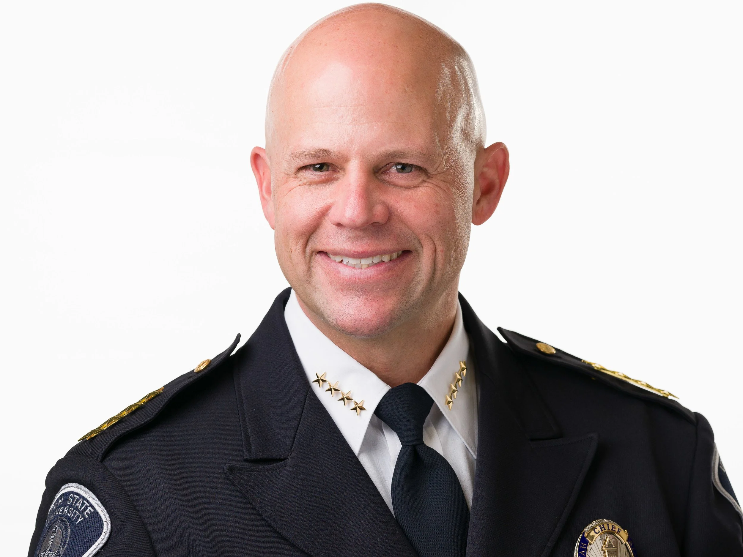 Portrait of a Blair Barfuss in a police uniform with gold stars on collar and shoulder epaulets, and a badge that says 'Chief'.