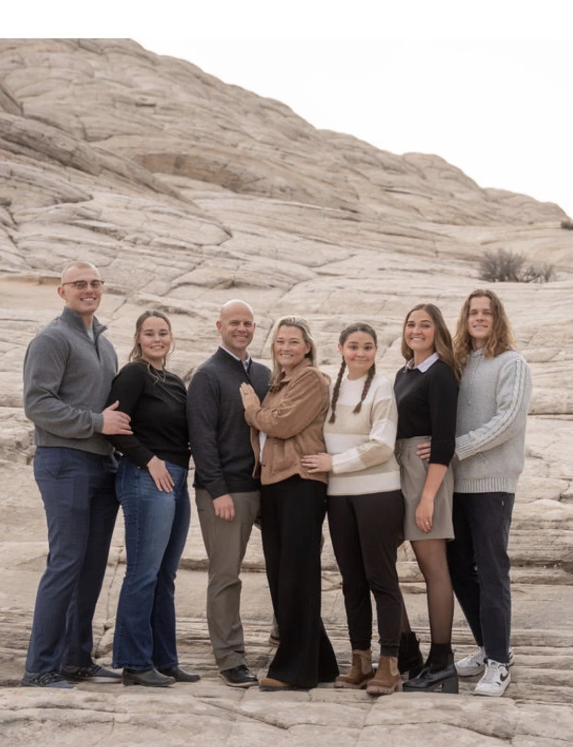 A group of seven people standing outdoors on rocky terrain with a large rock formation in the background, smiling and posing for the photo.