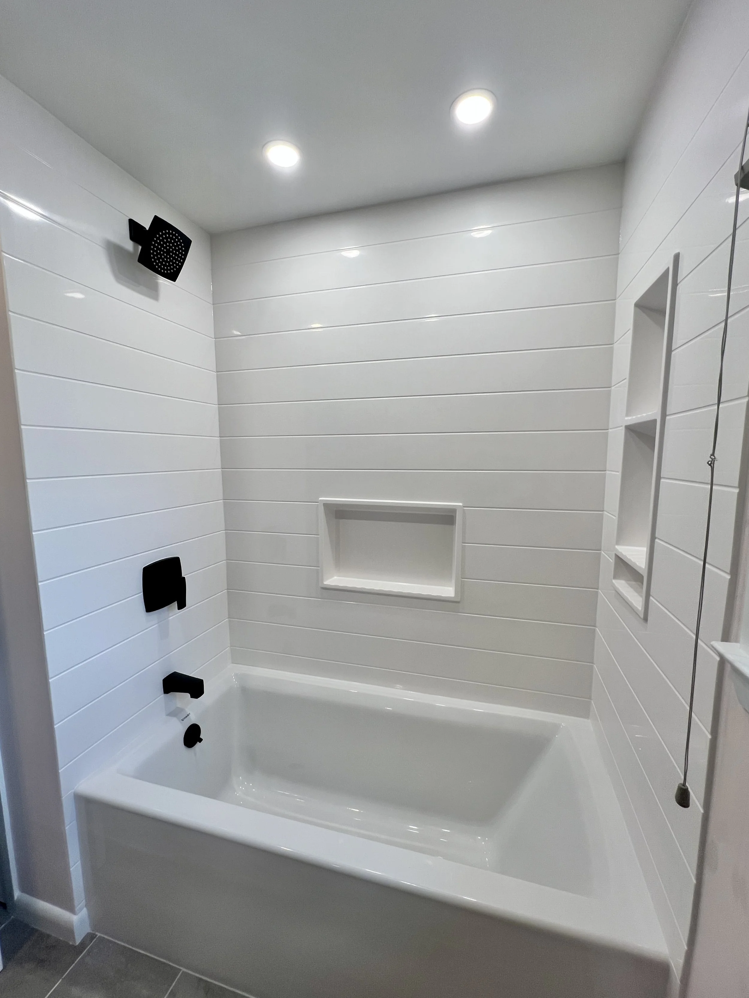 Modern bathroom shower with white tiled walls, black fixtures, and two ceiling lights.