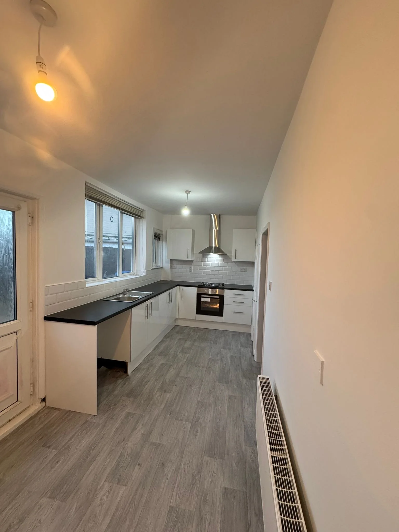 Fully renovated modern kitchen with white cabinets, black worktops, stainless steel extractor hood, tiled splashback, and grey wood-effect flooring