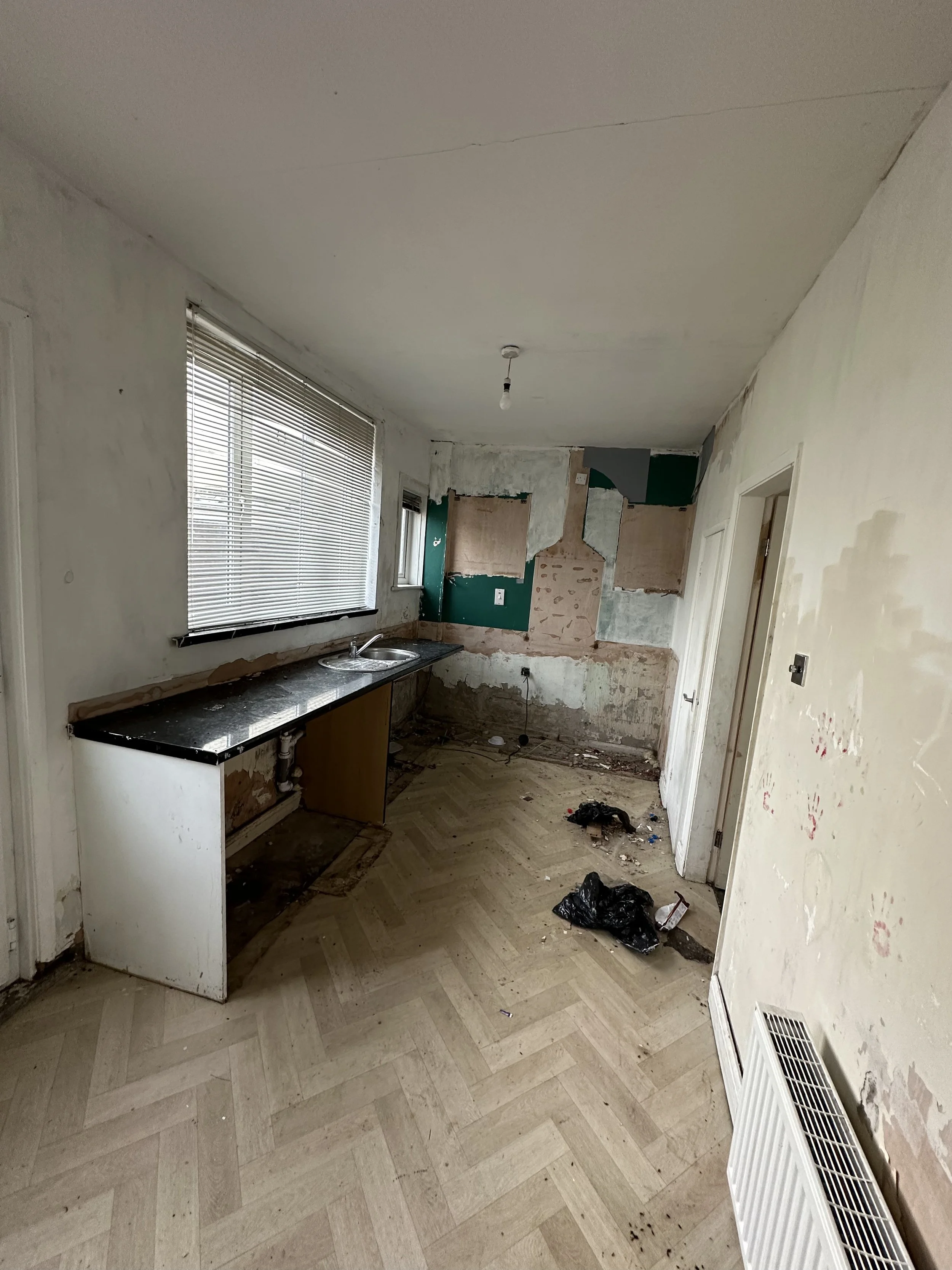 Dilapidated kitchen before renovation with damaged walls and old sink unit.